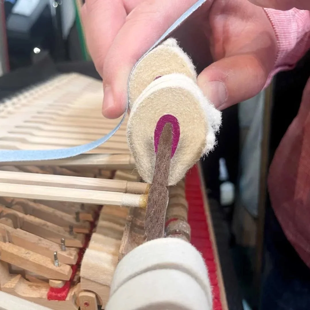 Nahaufnahme einer Person, die mit einem Messer eine raue, runde, beige-weiße Holzzunge schneidet, während das Innere eines Klaviers sichtbar ist.