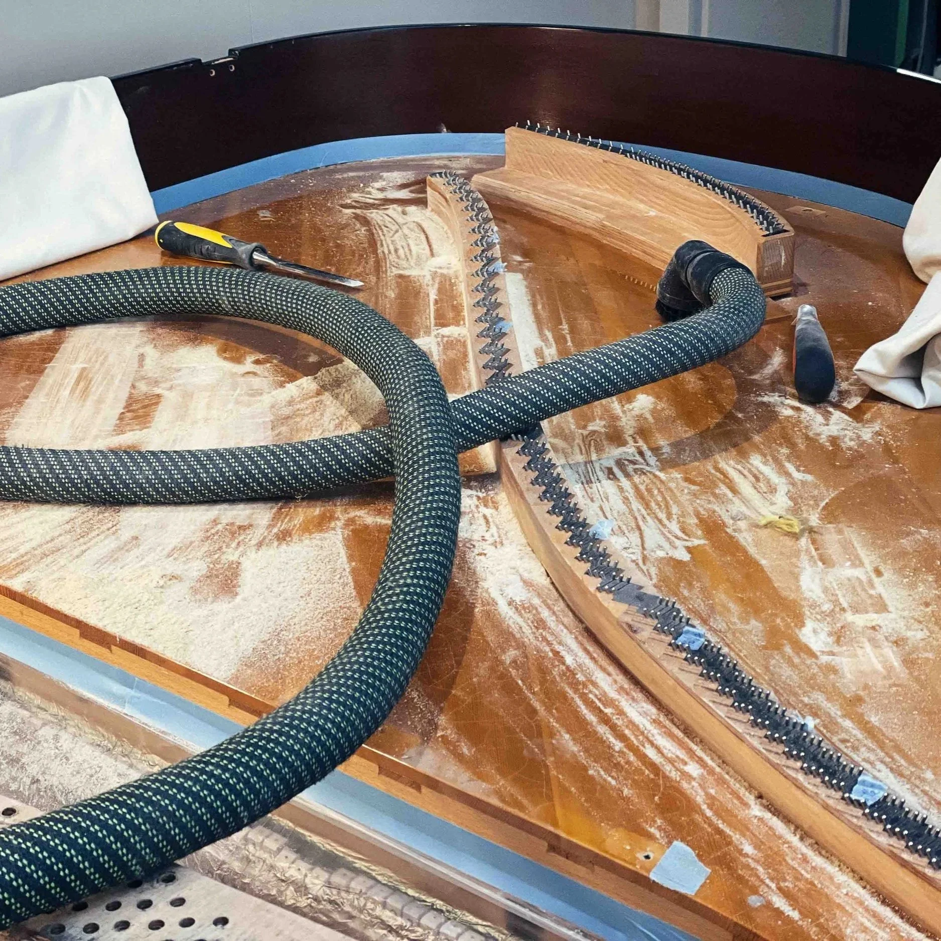 Innenansicht eines Klaviers während der Reparatur, mit Staub, Schraubenzieher, Haken, Staubsauger und Holzstücke im Inneren.