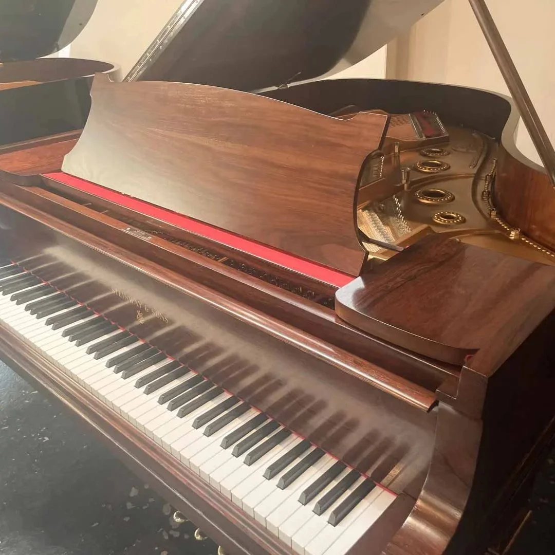 Ein Klavier mit offenem Deckel, das Holz ist poliert, die Tasten sind schwarz und weiß, das Innere des Klaviers ist sichtbar, mit goldfarbenen Saiten und Haken.