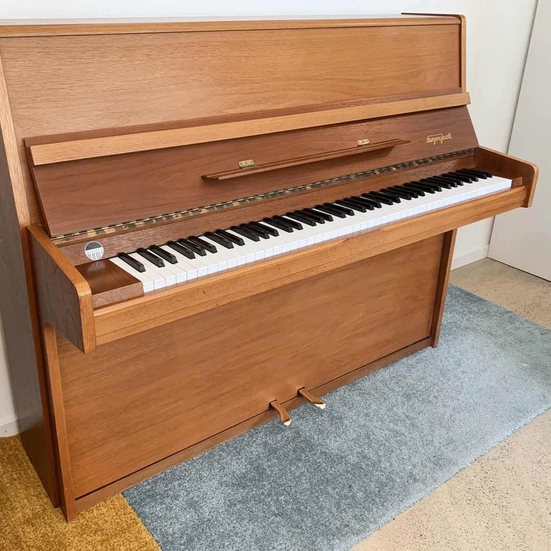 Ein hölzerner upright Klavier mit weißen und schwarzen Tasten, auf einem Teppich steht es in einem Raum.