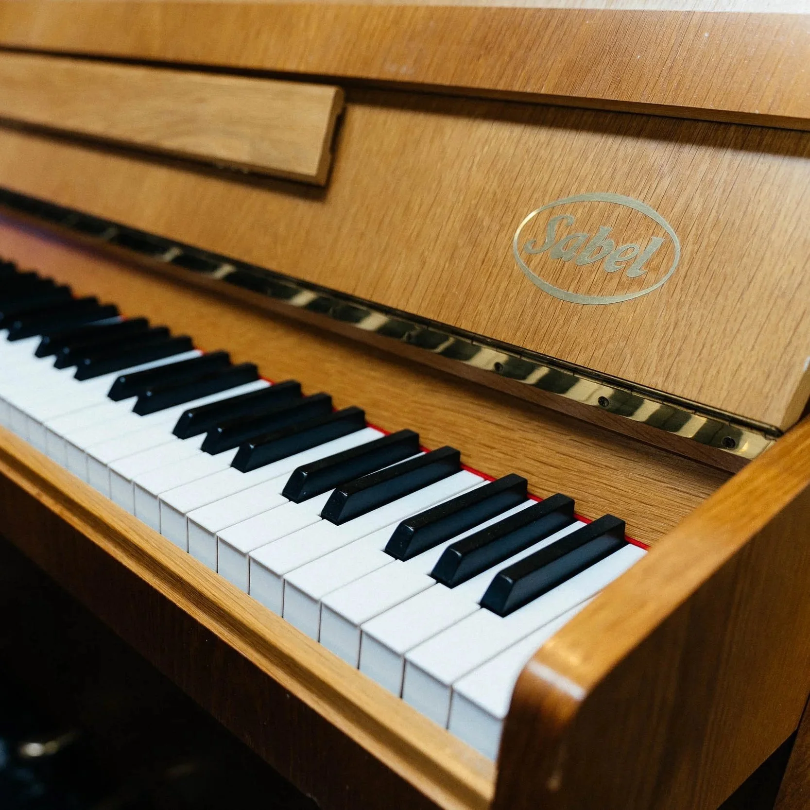Ein Klavier mit Holzgehäuse und schwarzen und weißen Tasten, das eine Marke namens "Sabel" trägt.