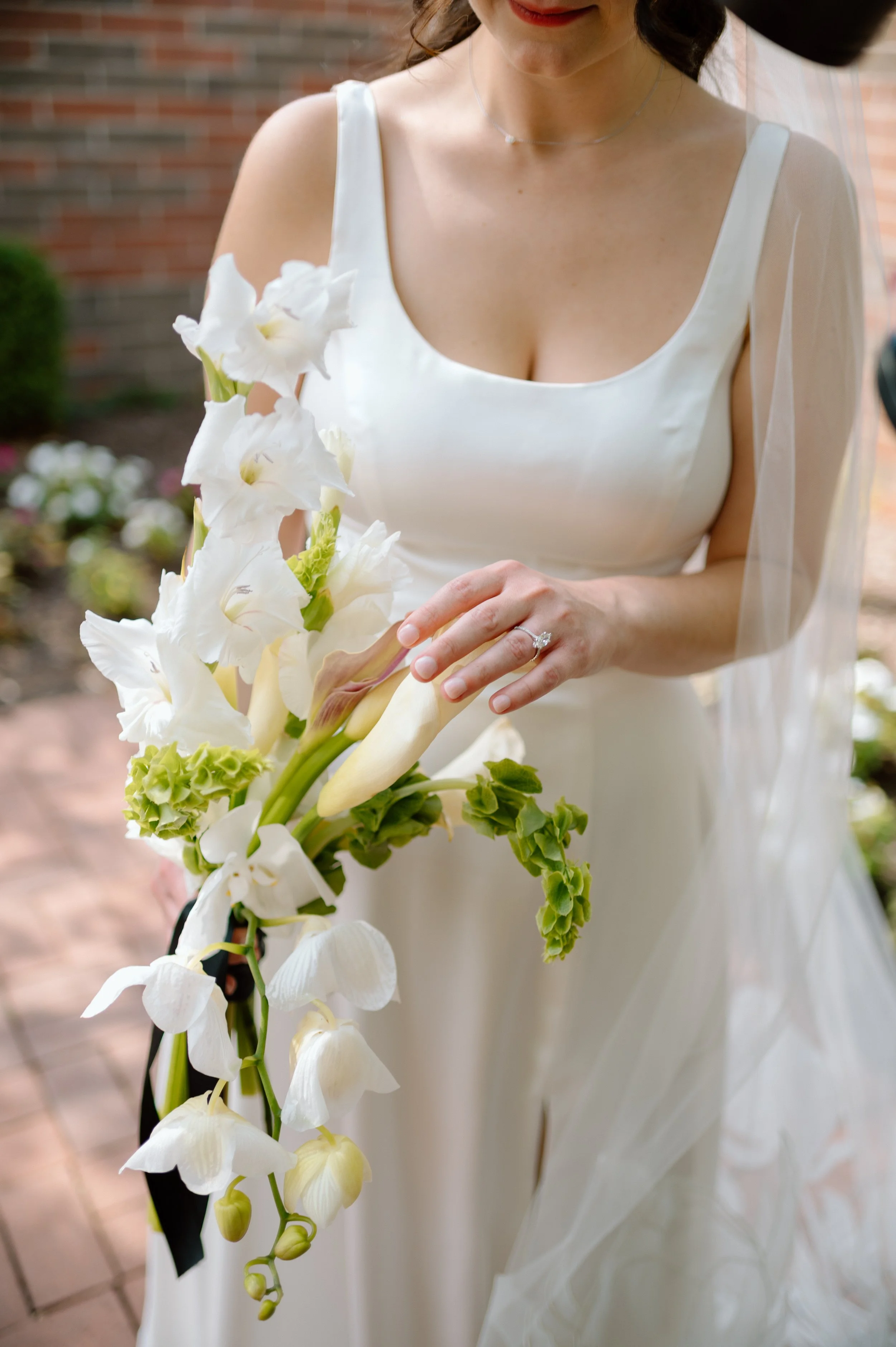 Bride in white wedding dress holding a cascading bouquet of white flowers, including calla lilies and orchids.