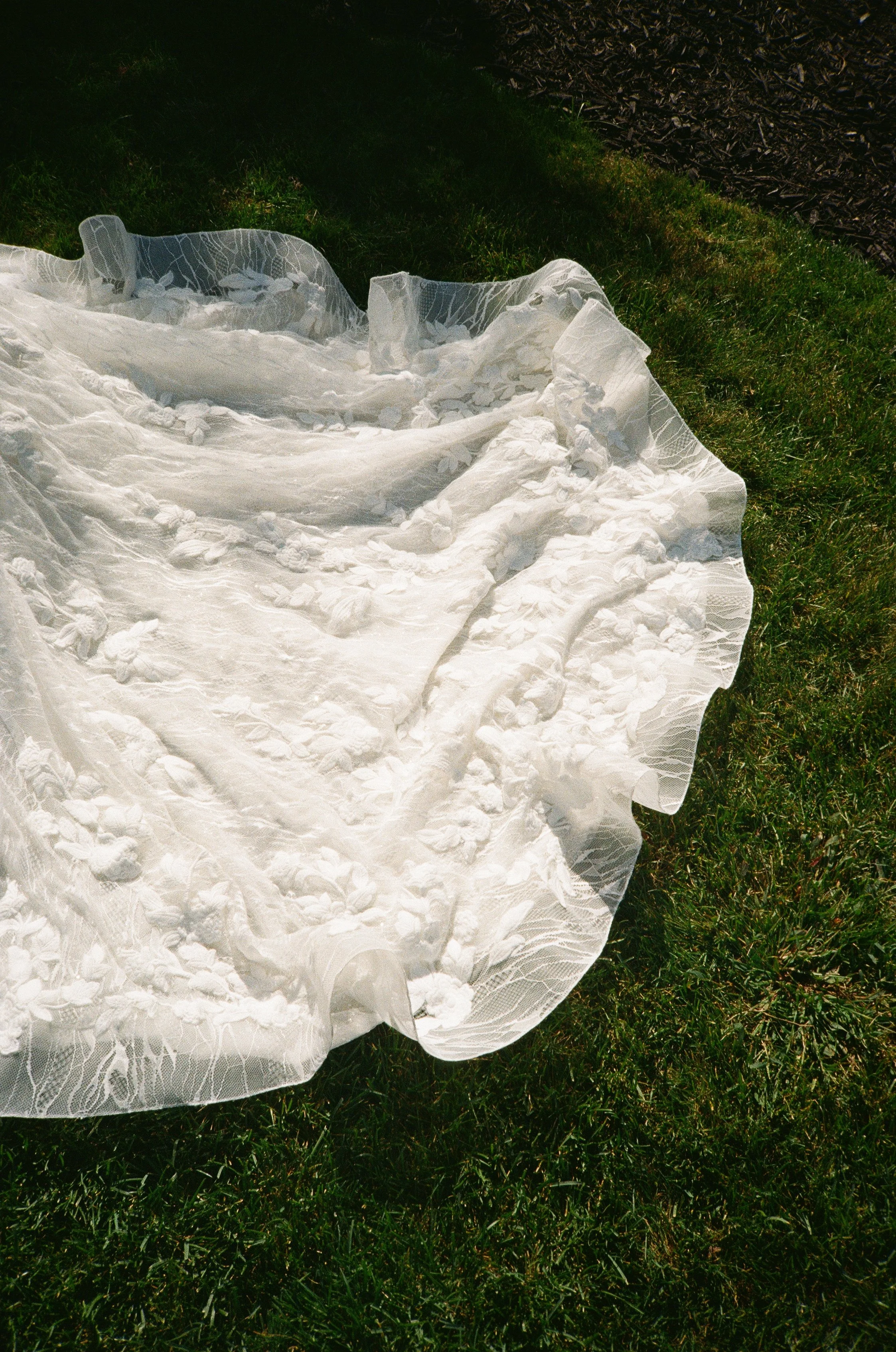 A white lace dress with floral patterns laid on green grass.