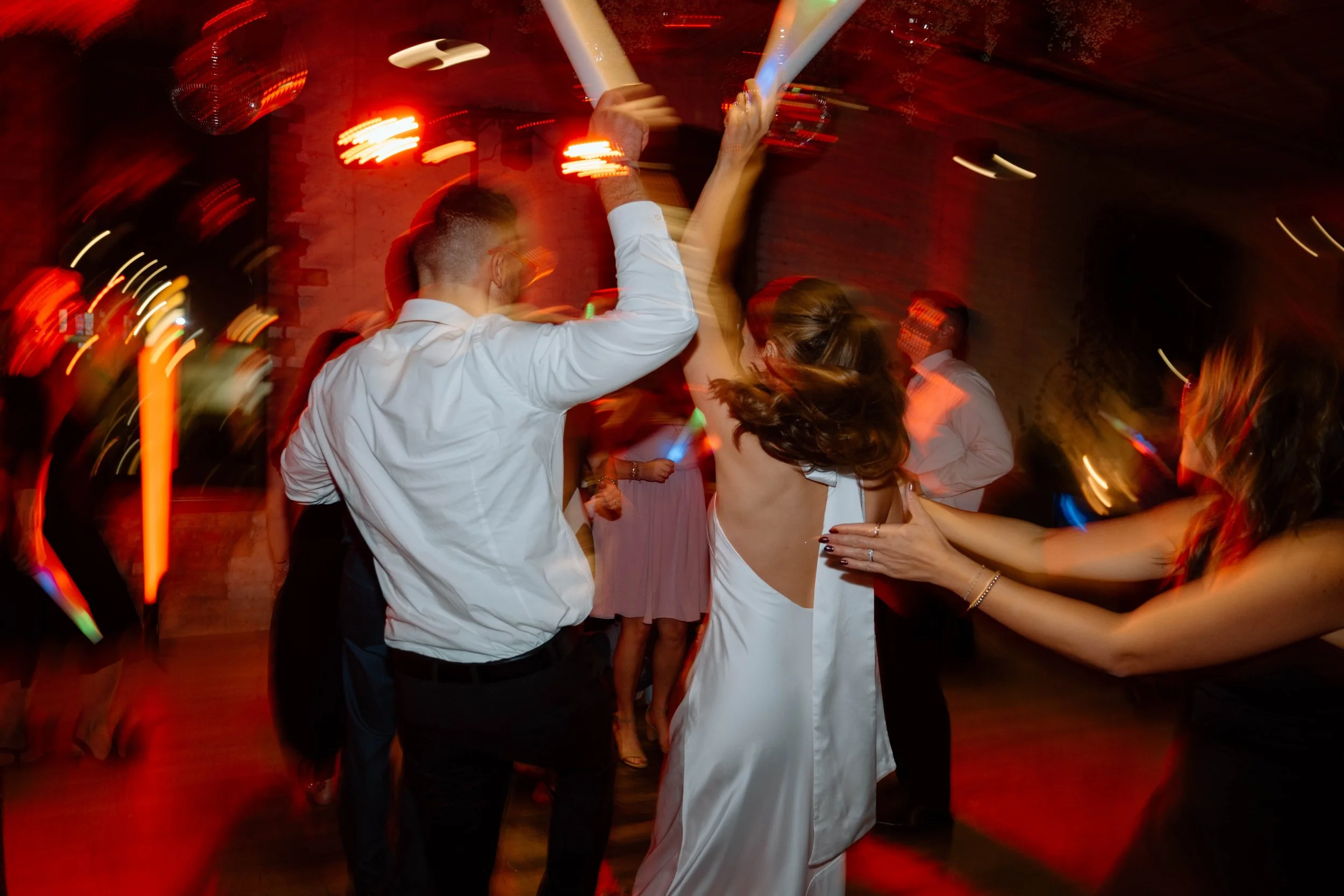 People dancing at a lively party with colorful lights and a brick wall background.
