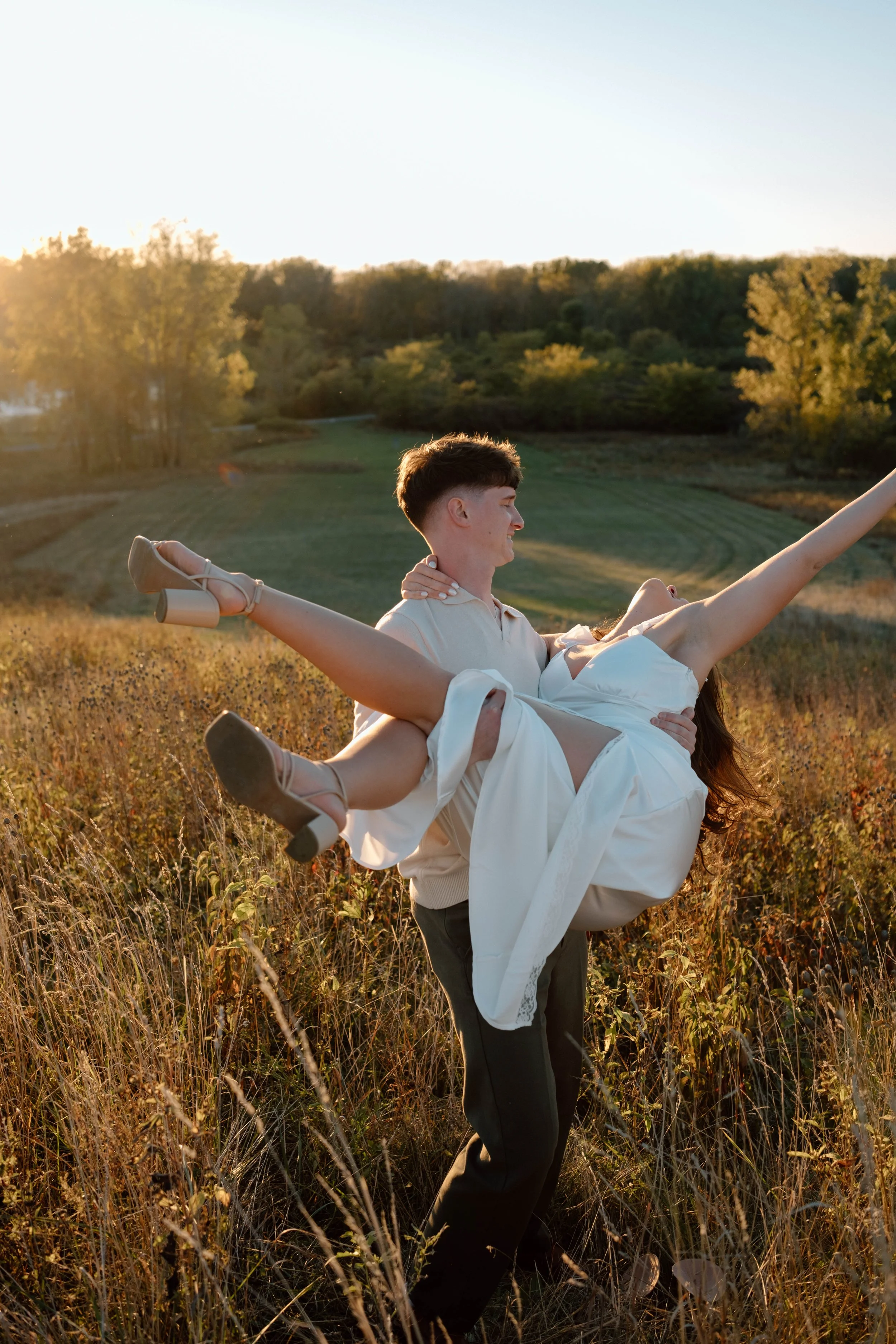A man lifting a woman in a field during sunset at Maumee Bay State Park in Ohio.