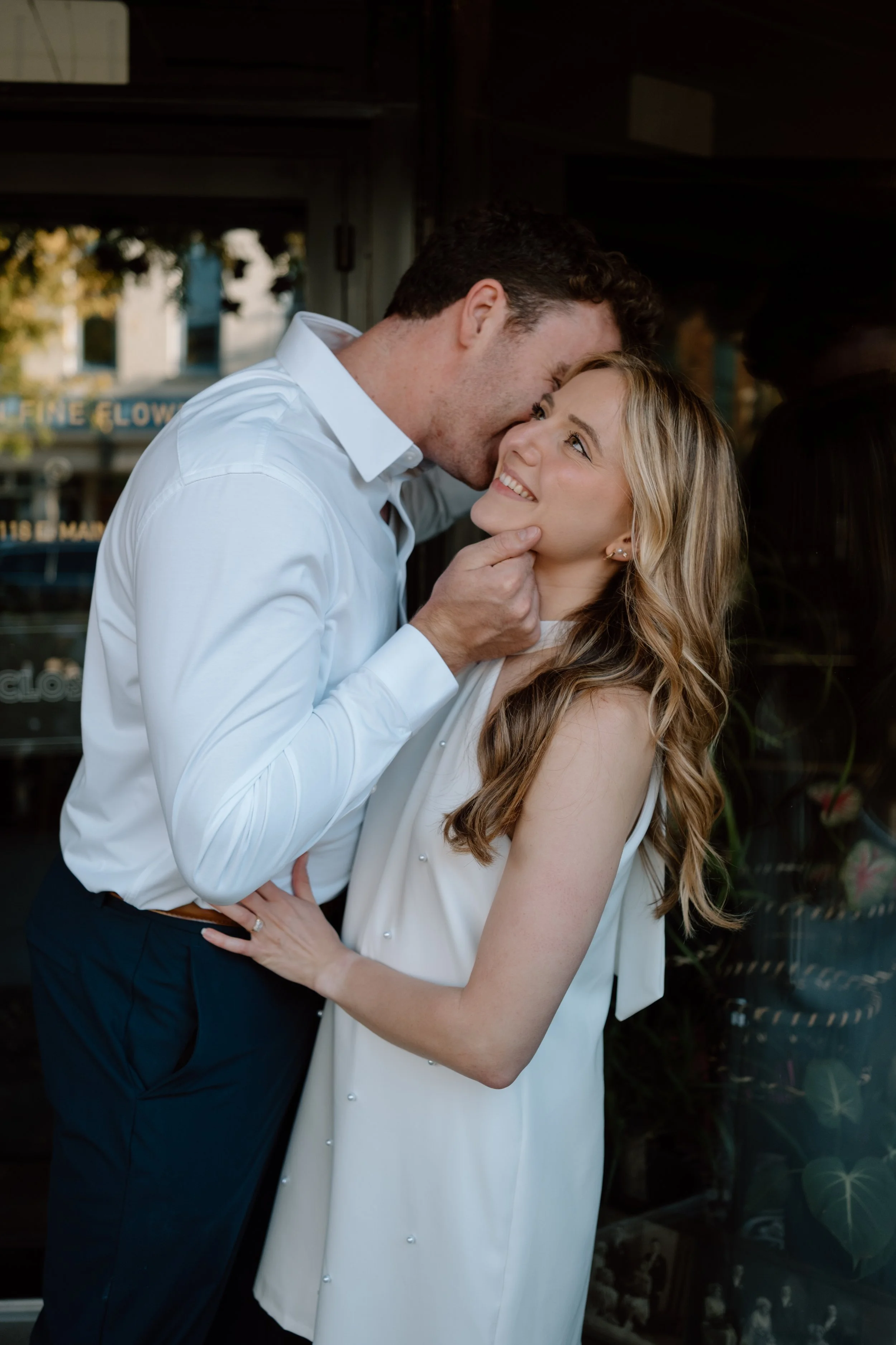 A man and woman sharing an intimate moment, with the man gently touching the woman's chin, both smiling and looking into each other's eyes.