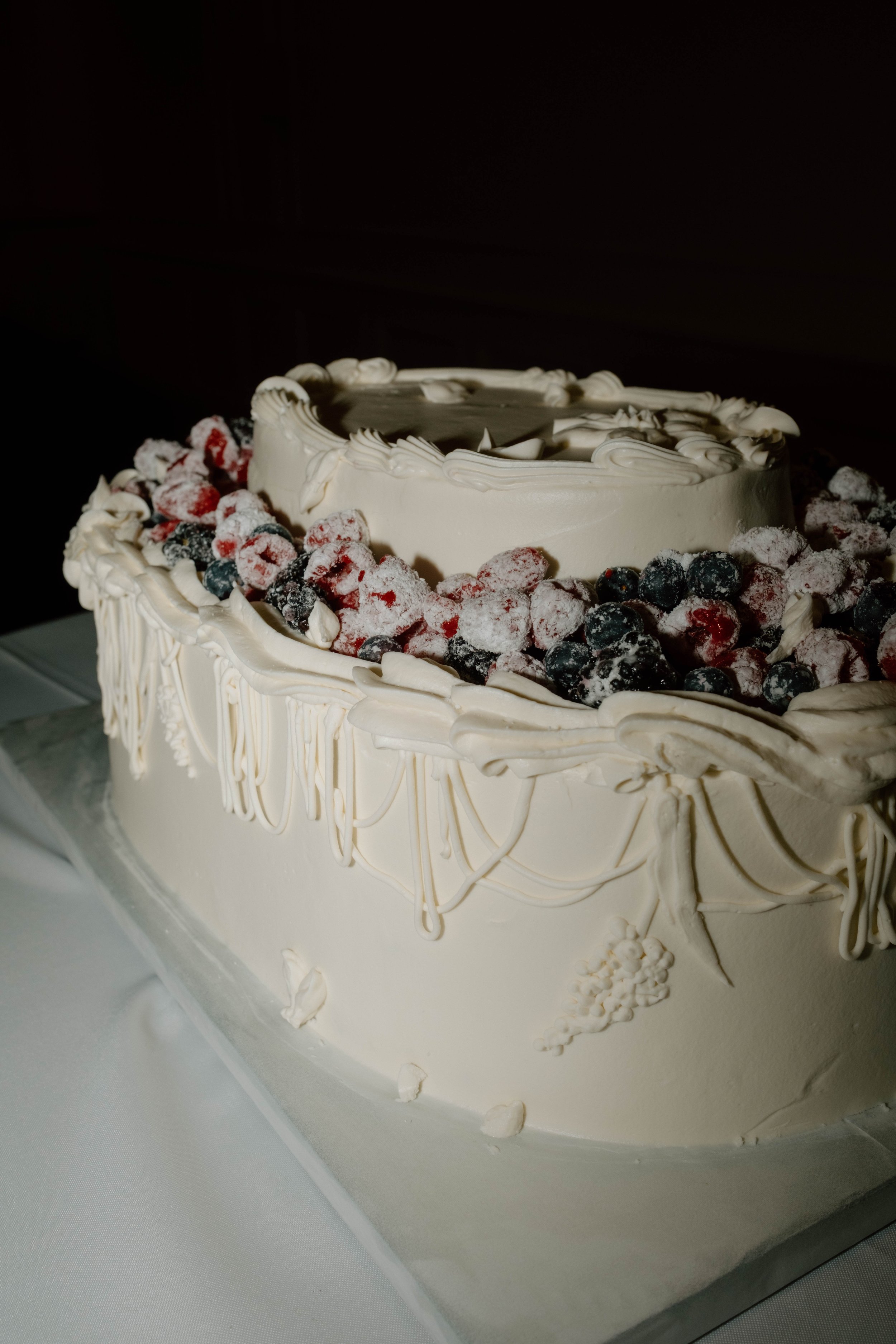 White wedding cake decorated with berries and white icing piped in swirls.