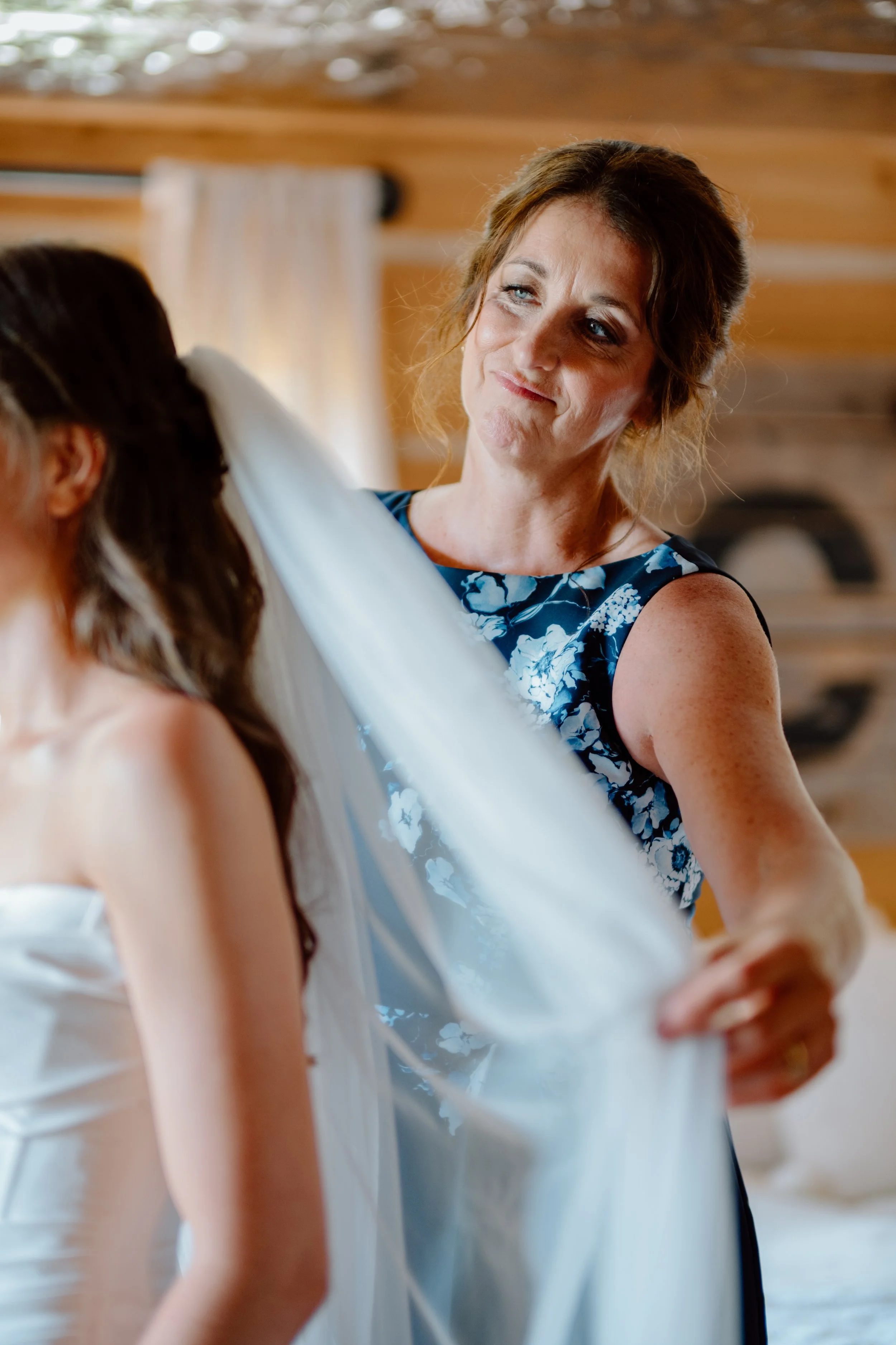 A mother helping a bride with her veil at a wedding inside a wooden cabin.