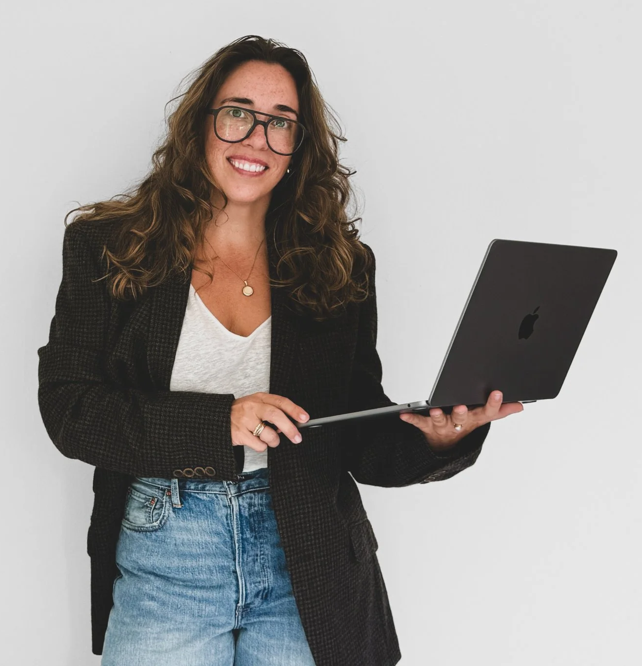 Brianna Albrecht Virtual In-Person Chicago Personal Stylist, Begin Anew wearing glasses, dark blazer over white top paired with jeans, holding open laptop