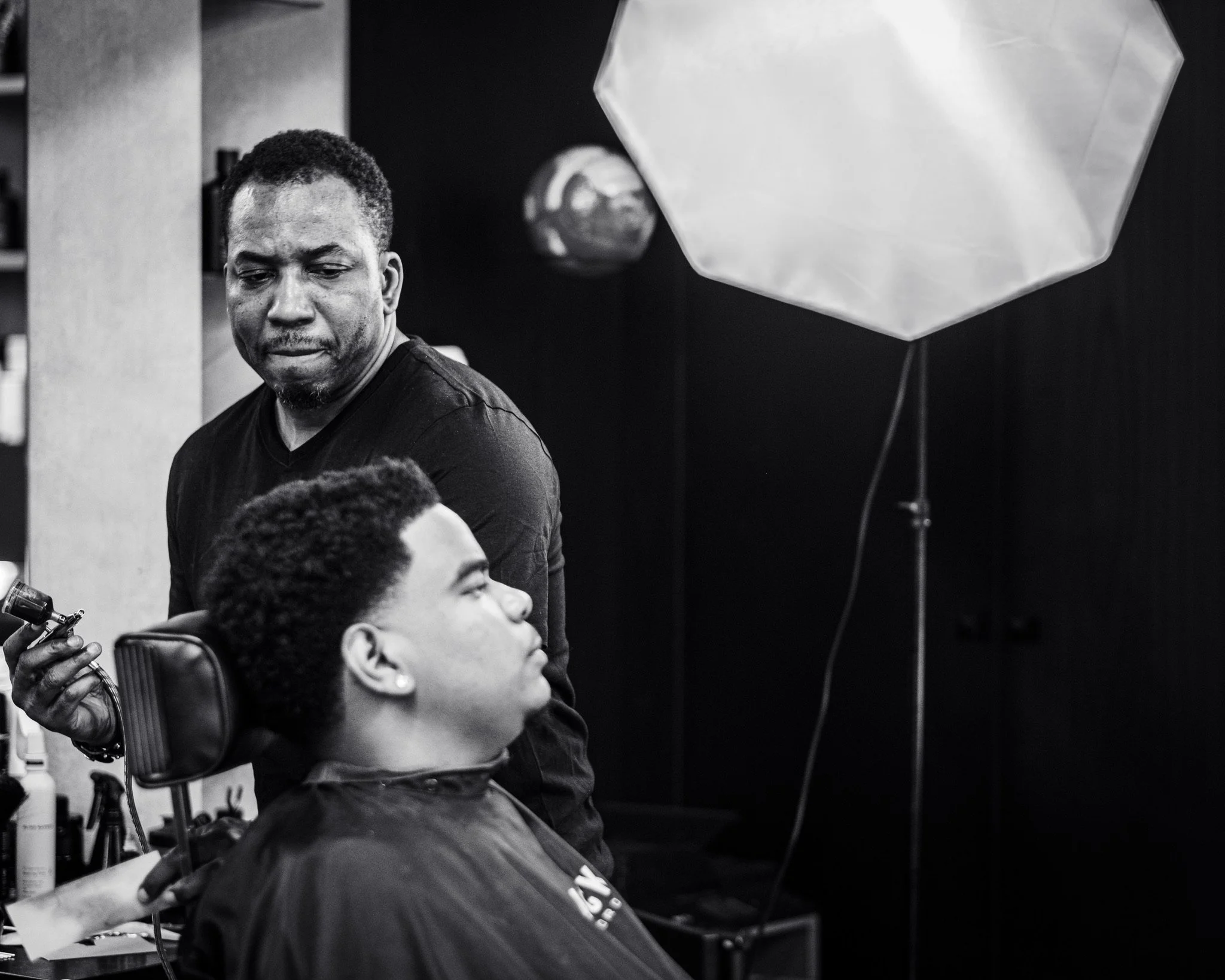 A group of people, including a man with short curly hair and a beard, in a professional or studio setting with photography equipment and a large softbox light visible.