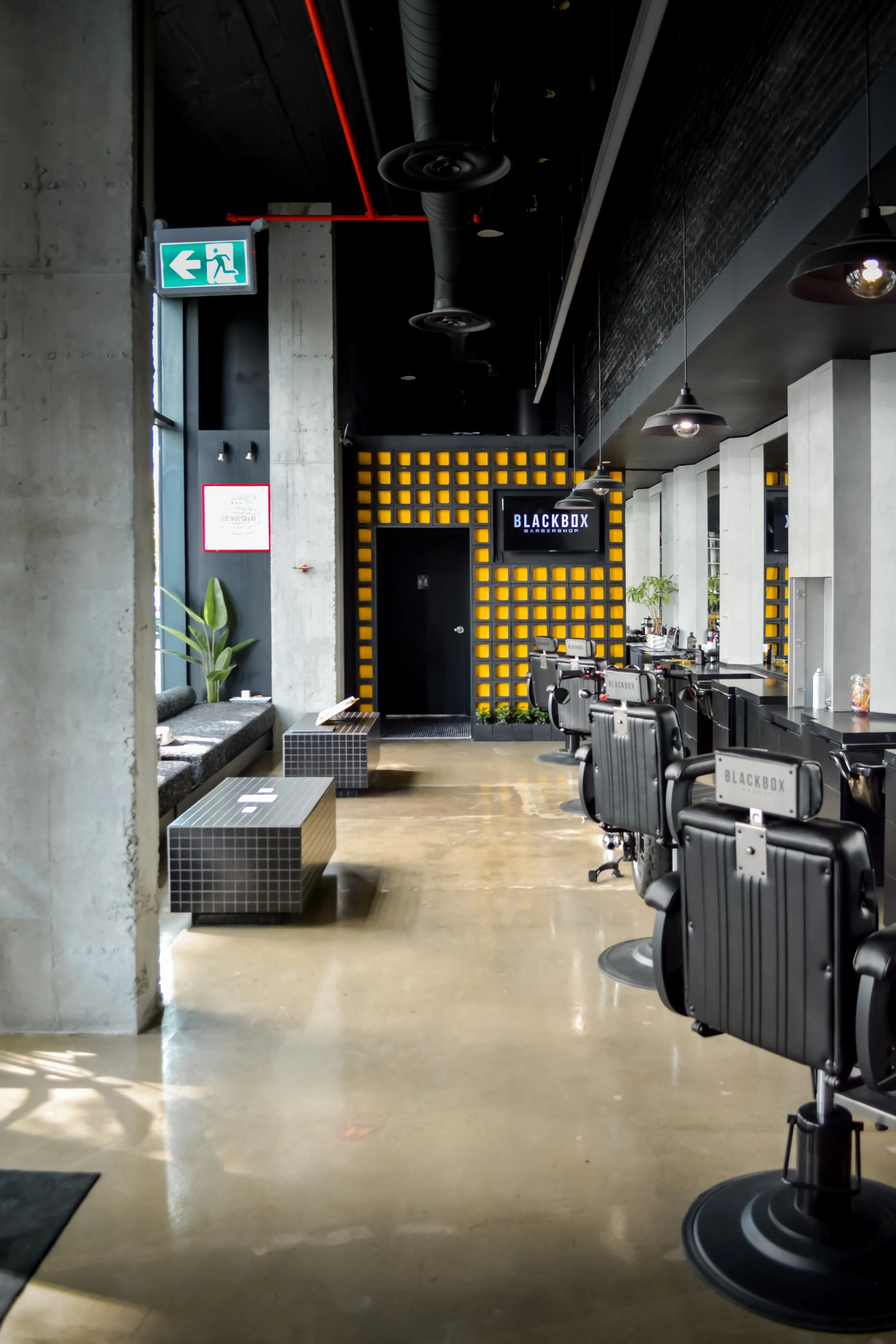 Interior of a modern barbershop with black barber chairs, a black and yellow decorative wall, and a sign that reads 'BLACKBOX BARBERSHOP'.