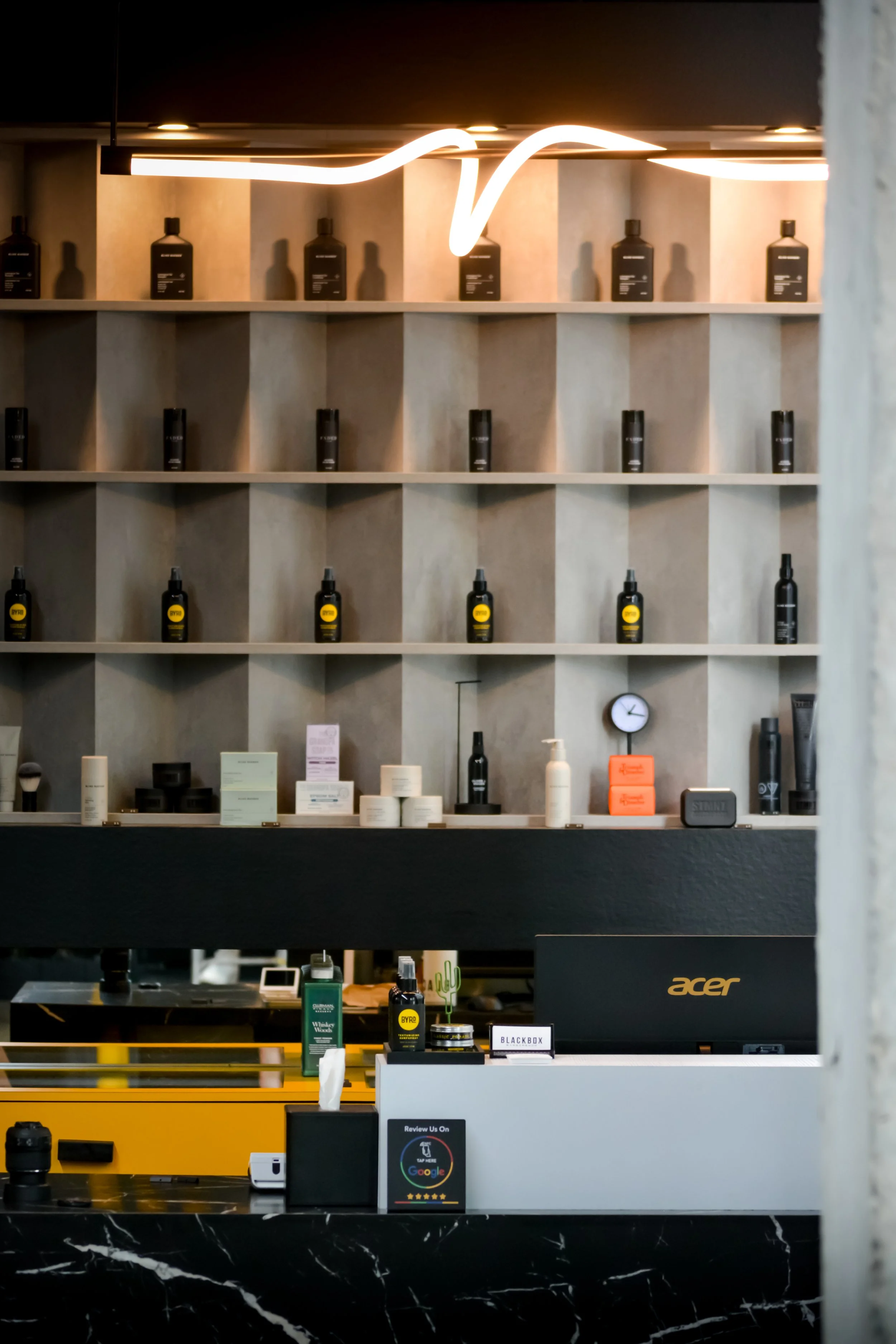 Indoor retail display with shelves of skincare and beauty products, neon light fixture, and checkout counter with small items and review sign.