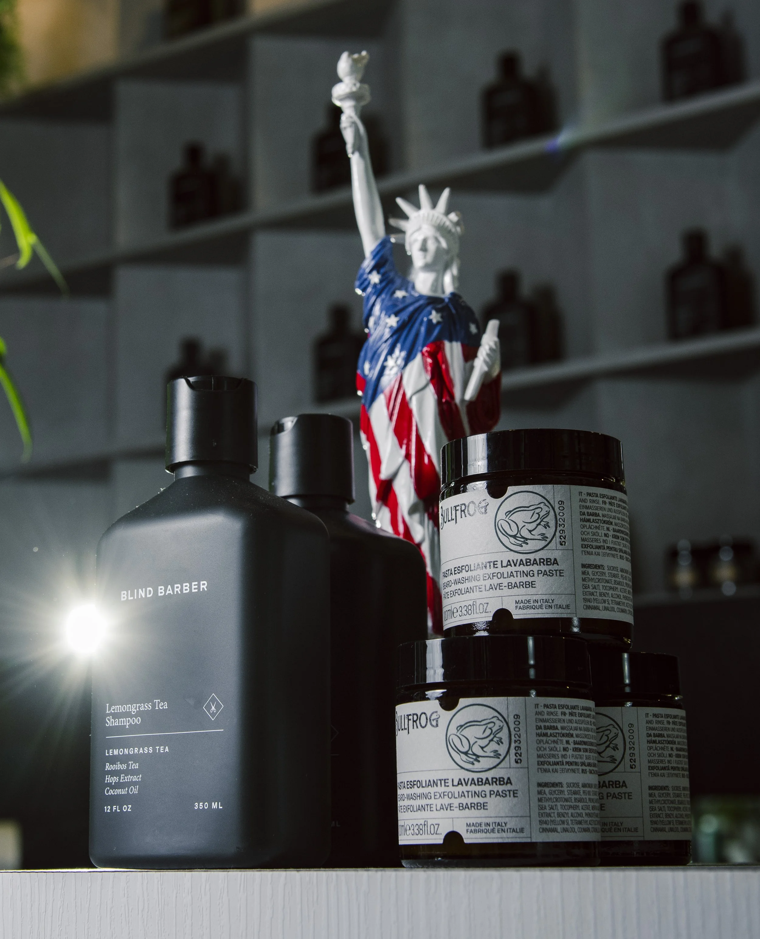Small decorative American flag in the shape of the Statue of Liberty, placed among black bottles on a shelf, with a blurred background of storage shelves.