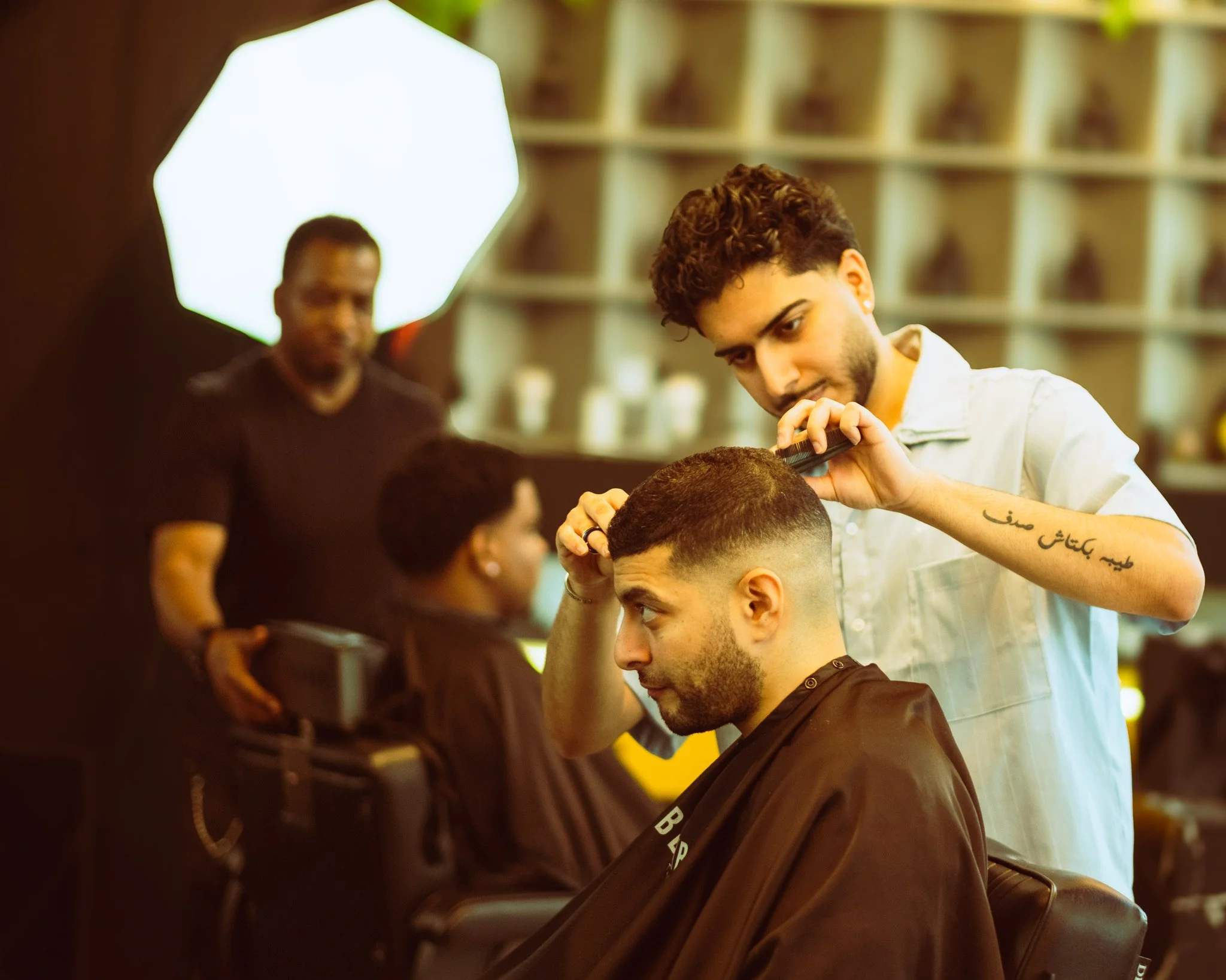 Barber cutting a client's hair in a barbershop with shelves in the background.