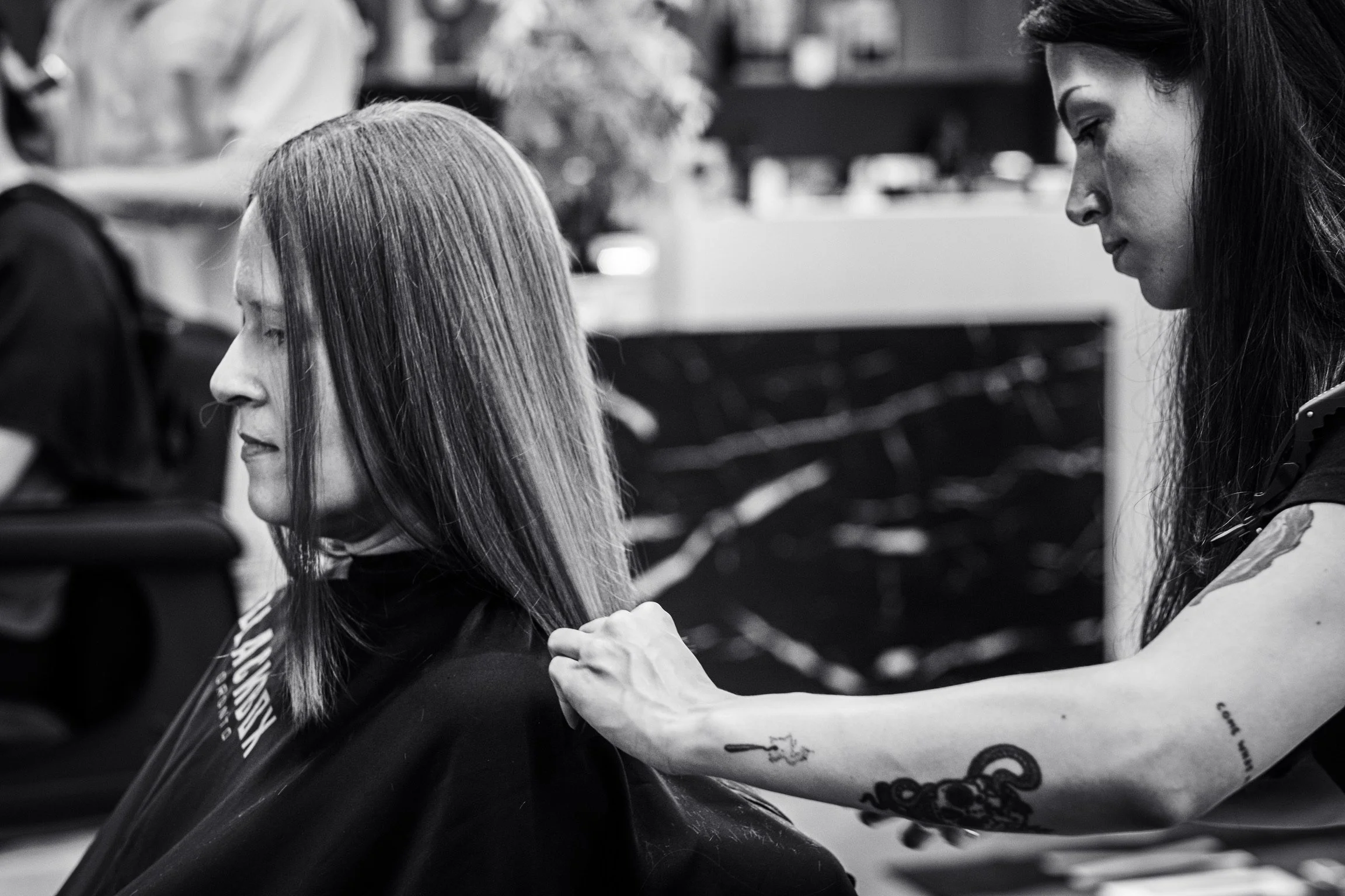 A woman with long hair receives a shoulder massage from another woman with dark hair in a salon or spa setting.
