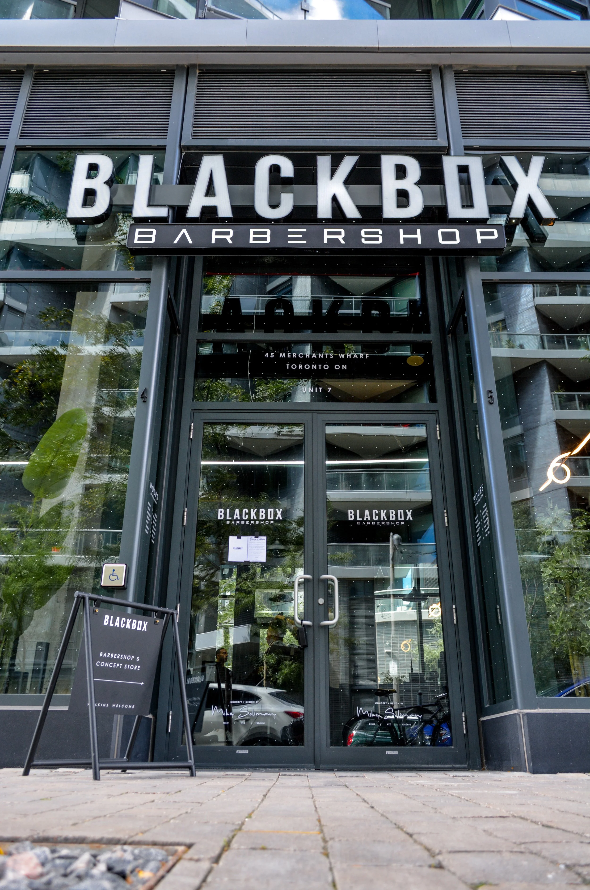 Front entrance of BLACKBOX Barbershop with glass doors and signage, located at 45 Merchants Wharf, Toronto.