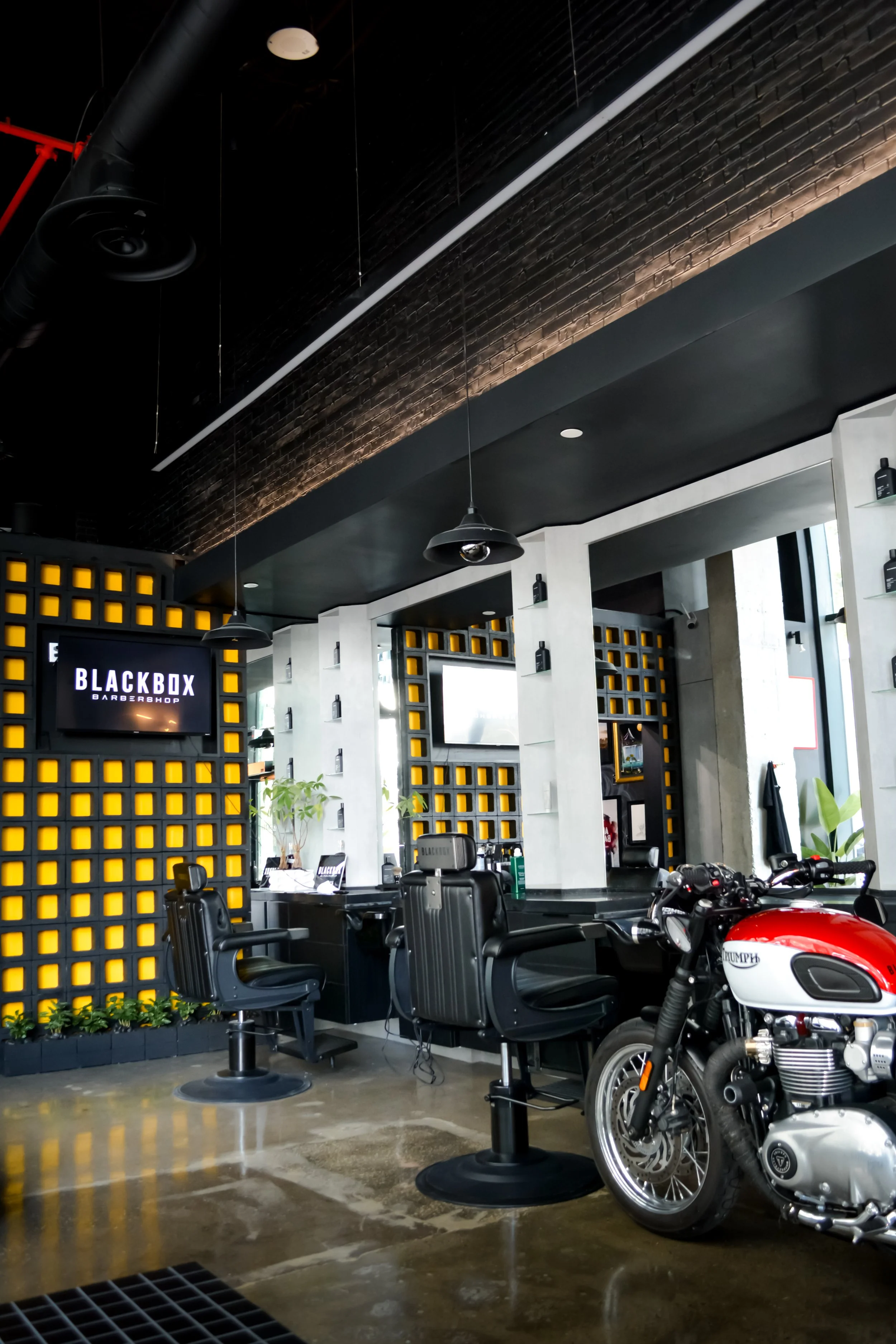 Interior of a modern barbershop with black and yellow decor, barber chairs, a motorcycle, and televisions on the wall.