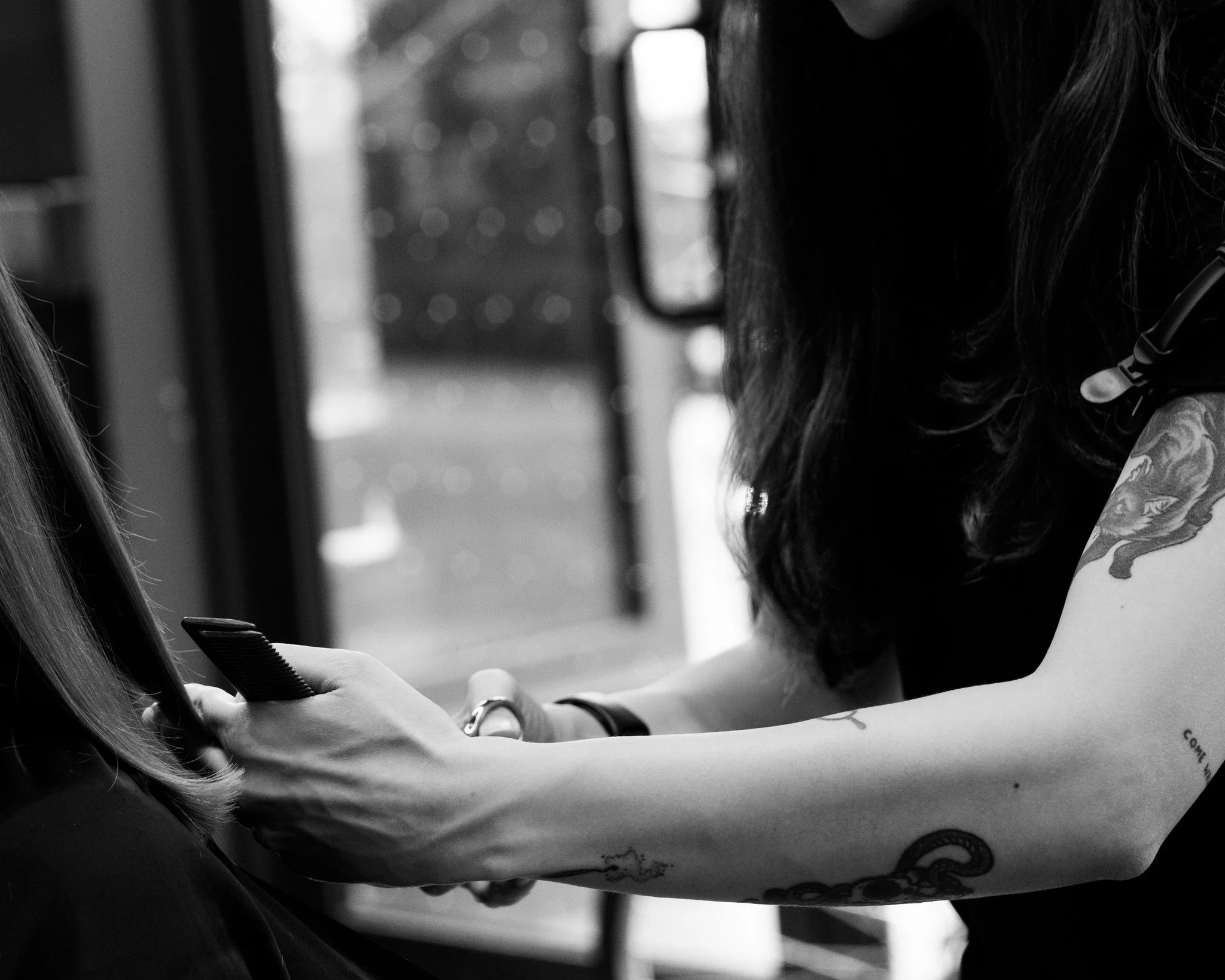 A woman with dark hair and tattoos on her arm, wearing a headset, is receiving a tattoo from another woman with long hair.