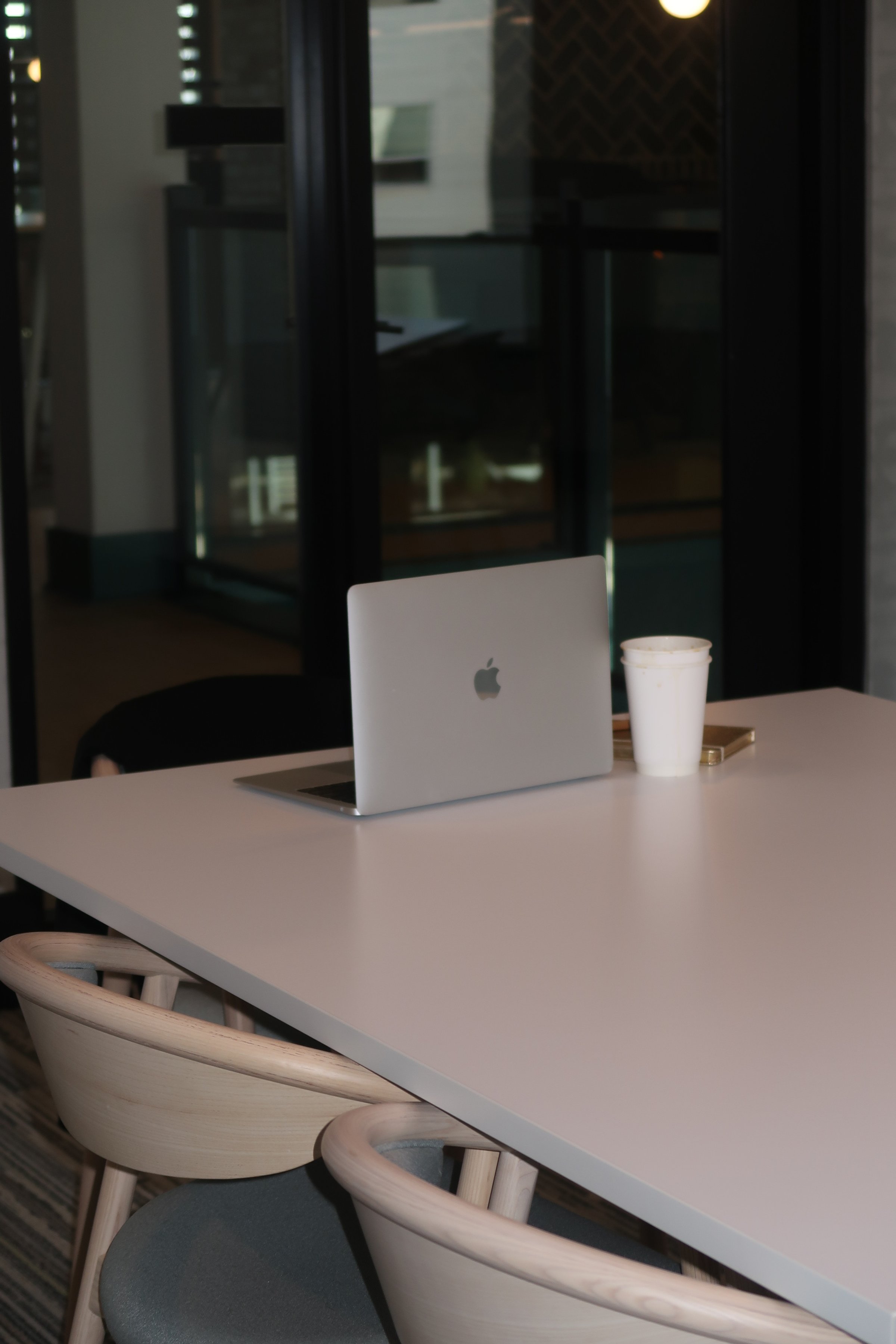 A laptop, a white disposable cup, and a smartphone on a white table in a modern office or cafe setting.