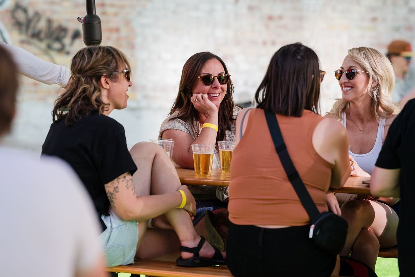 Group of women sitting at a table outdoors, socializing and drinking beer.