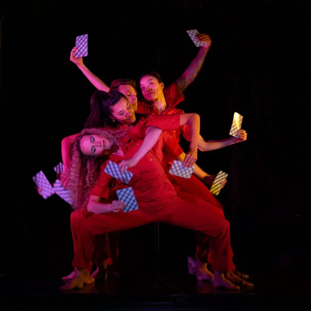 Group of dancers in red costumes holding checkered fans, performing on stage with a dark background.