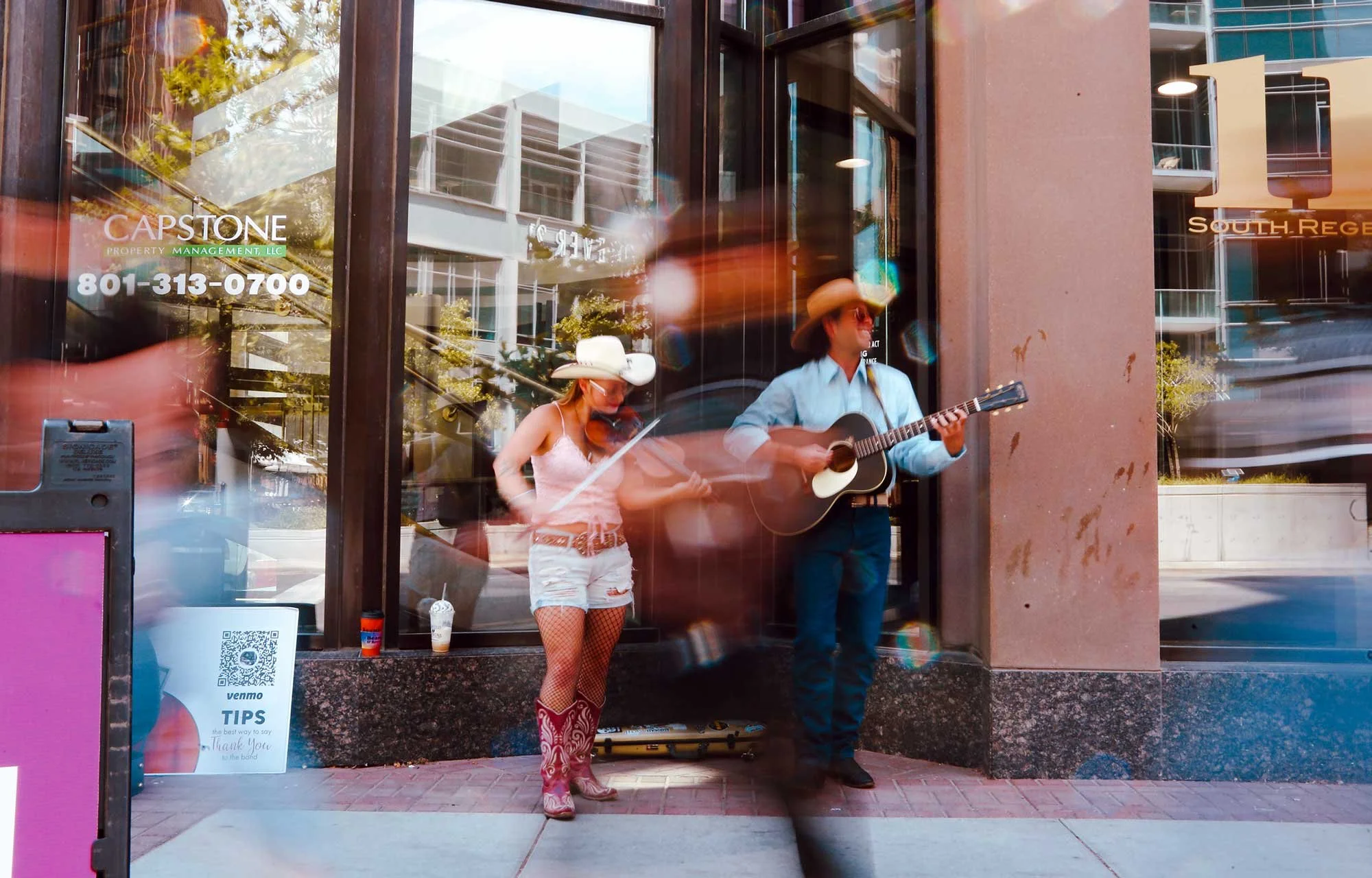 A woman plays the violin while a man plays the guitar while busking in downtown Salt Lake City.