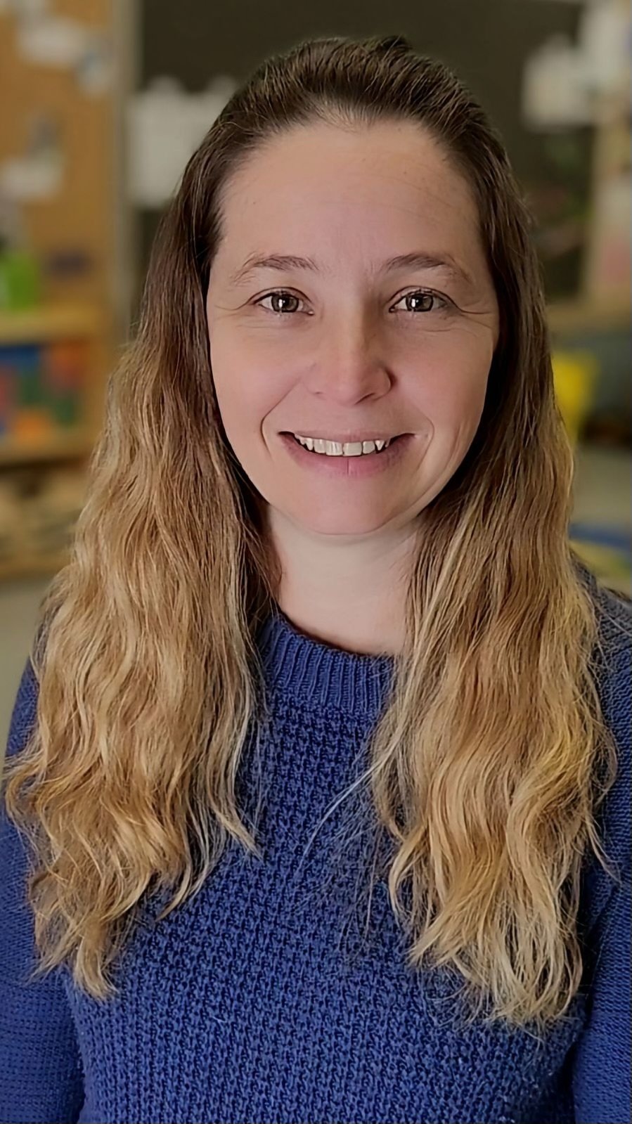 Smiling woman with long hair wearing a blue sweater indoors.