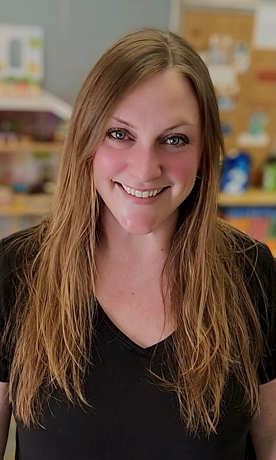 Smiling woman with long hair wearing a black shirt in a classroom setting.