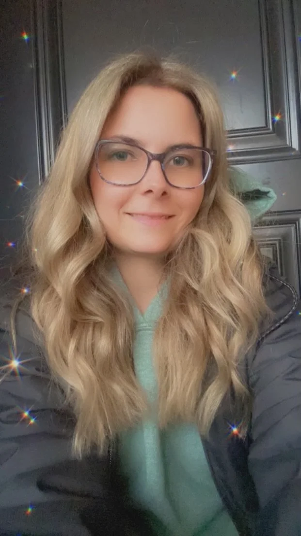 Woman with long wavy hair and glasses smiling indoors.