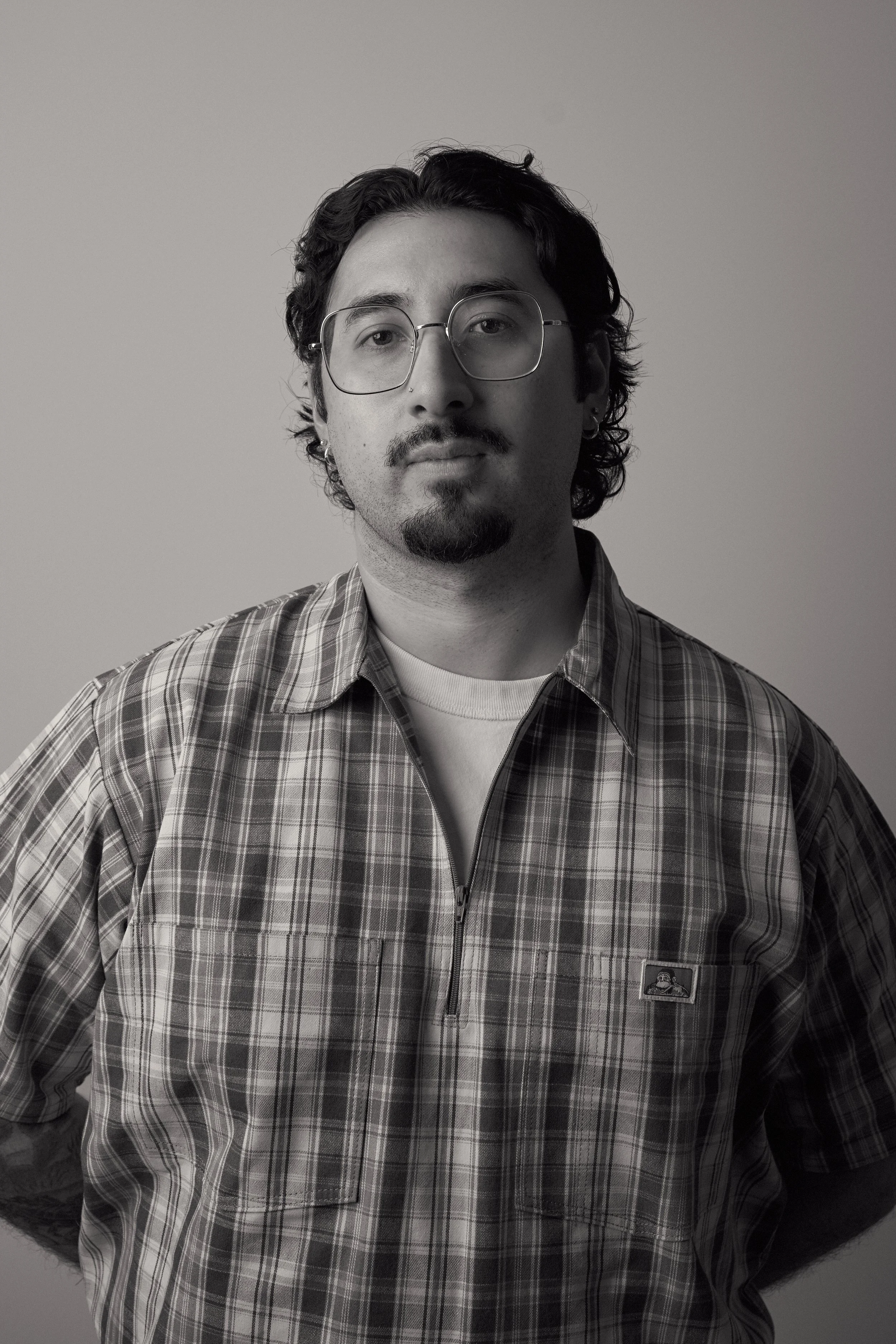 Black and white portrait of a man wearing glasses, a plaid shirt, and a white undershirt, against a plain background.