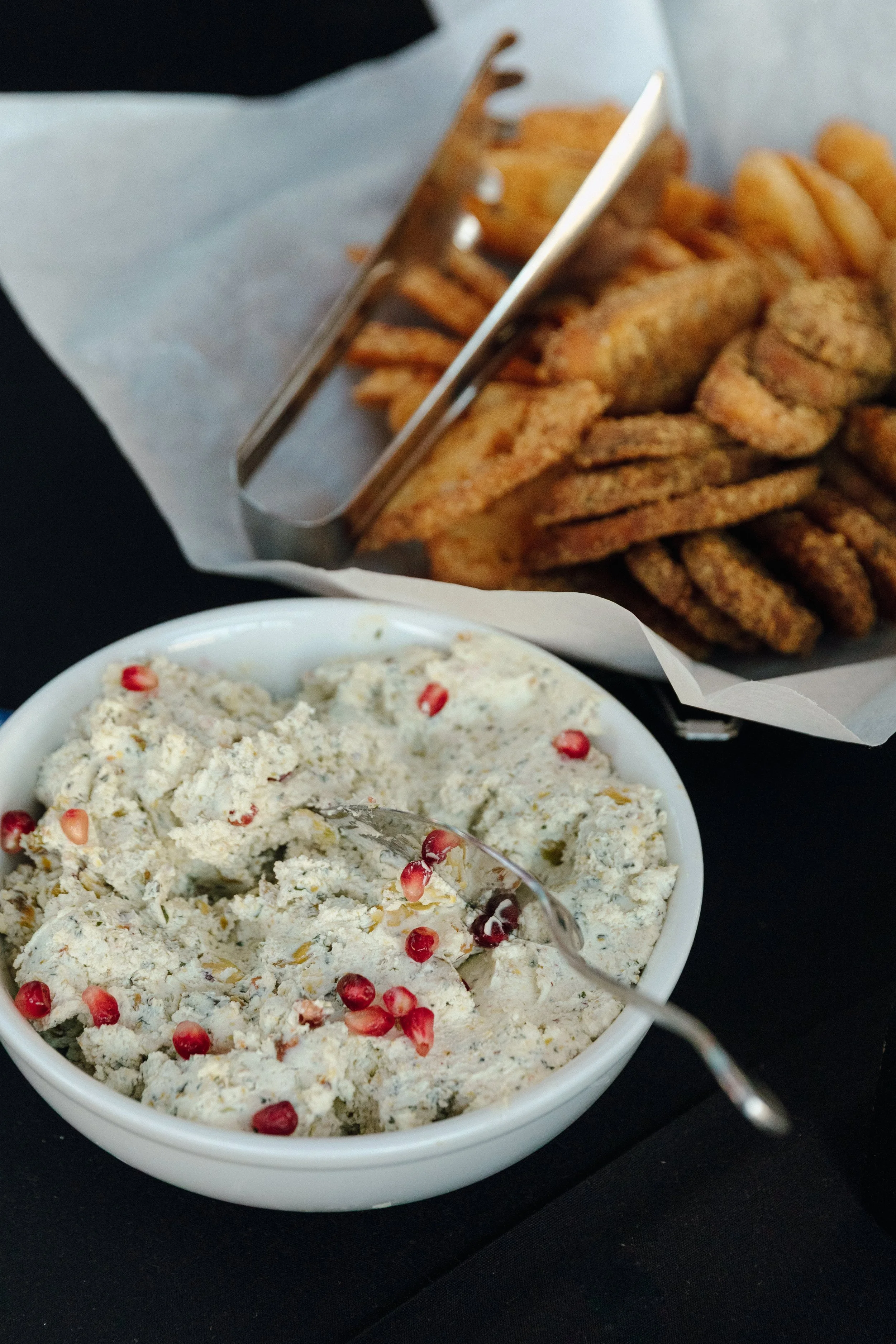 Appetizers private event with a bowl of creamy dip topped with pomegranate seeds and a spoon, with a basket of fried chicken and onion rings in the background at Bassett Hound, Minneapolis in North Loop Green.