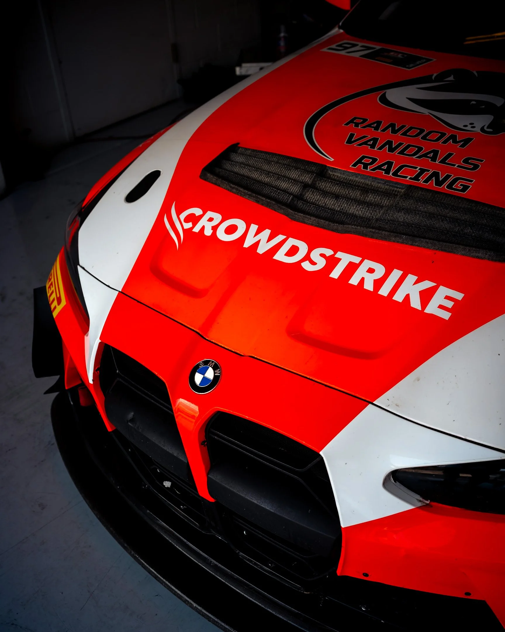 Close-up of a racing car with BMW logo, red and white livery, and decals including 'Crowdstrike' and 'Random Vandals Racing'.