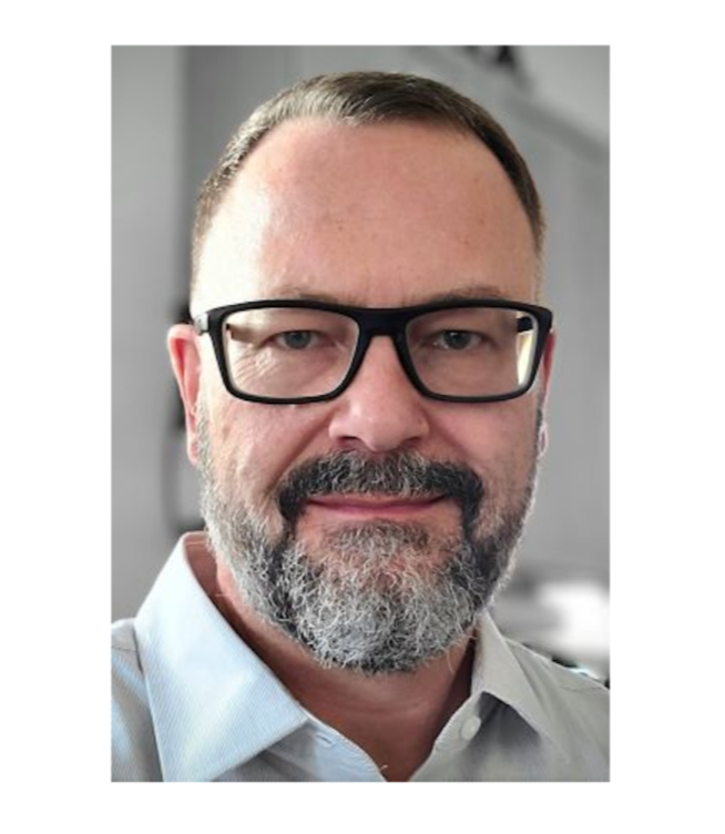 Portrait of Eric J. Blommel, MA, LPC, a Denver-based trauma therapist with glasses and a trimmed beard, wearing a light collared shirt.