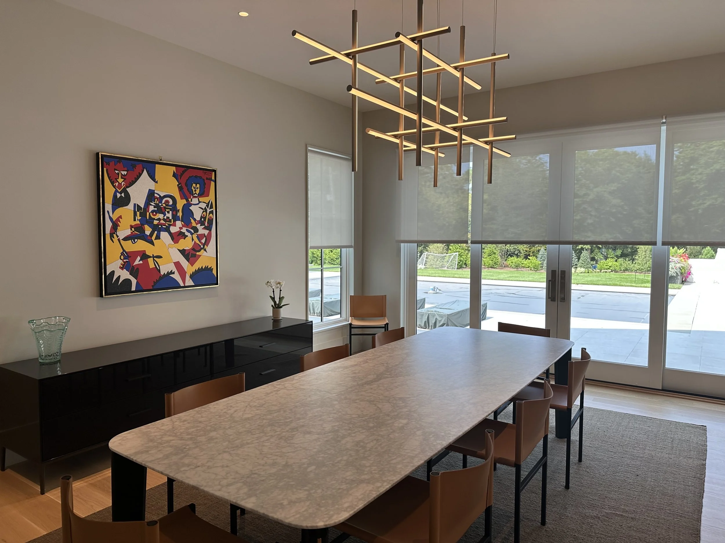 Modern dining room with a large marble table. Lutron Palladiom Shades cover all doors and windows in the room. All shades and lighting are controlled by Lutron HomeWorks QSX lighting control system