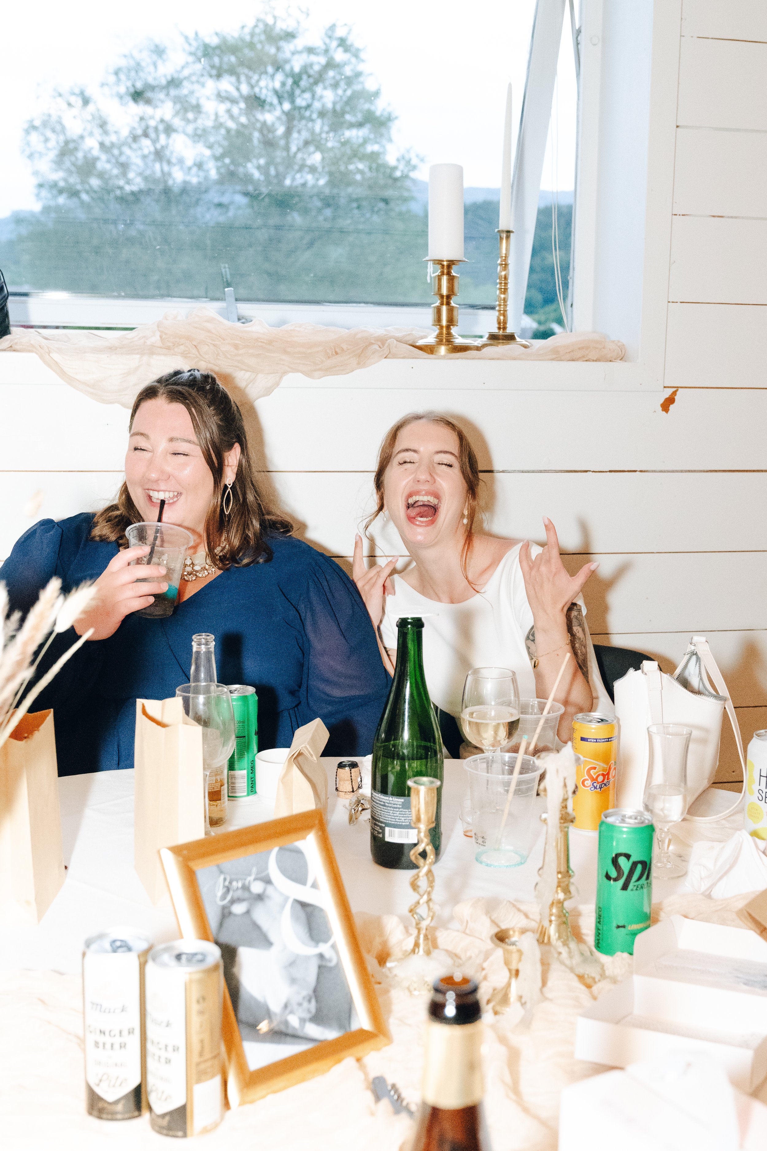 To kvinner som smiler og ler, nyter en bryllupsfest i haugesund anledning med drikker.