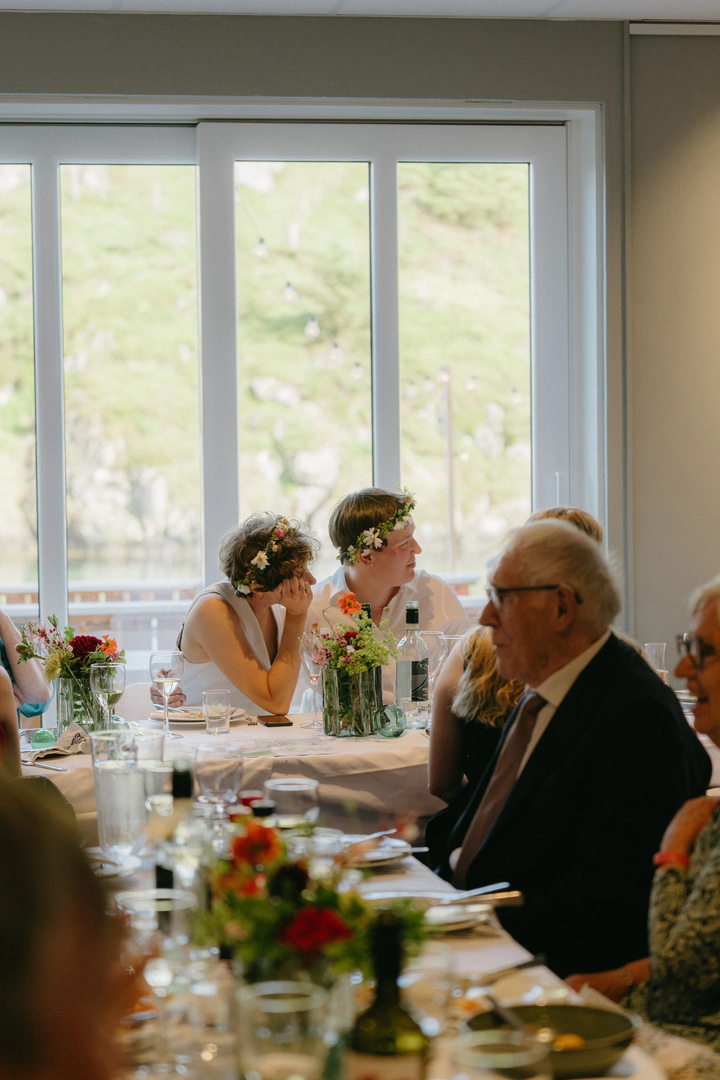 En kvinne i en brudekjole på Røvær gir en bukett blomster til en mann i en dress på en trapp med en hvit vegg og en blå himmel bak.
