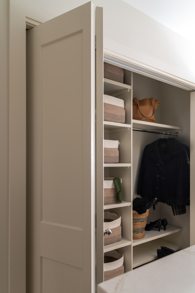 A look inside an open closet with organized shelves holding woven baskets, a brown leather tote bag, and a black jacket hanging on a rod.