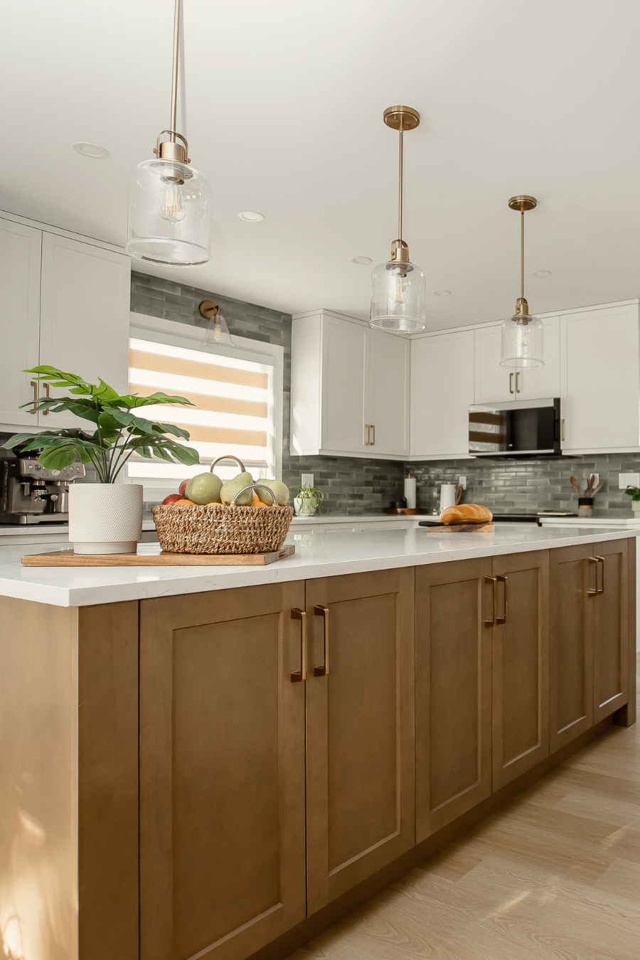 Modern kitchen with white upper cabinets, warm wood island cabinetry, gold hardware, quartz countertops, and glass pendant lighting, showcasing a bright and stylish contemporary kitchen renovation.