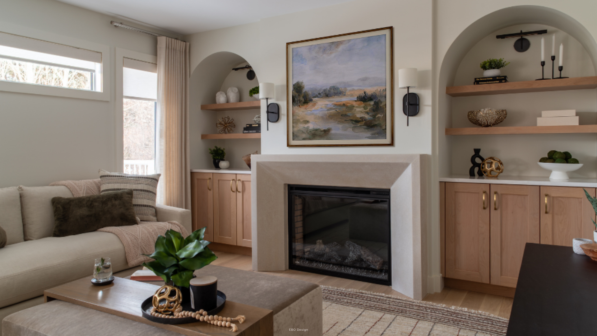 A transitional living room featuring a concrete fireplace, flanking arched wood built-in shelves with décor, a light wood coffee table, and a sofa with various throw pillows.