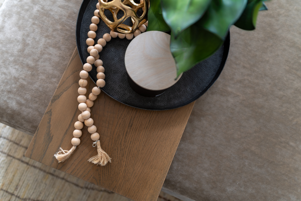 An overhead detail shot focusing on a decorative vignette on a wooden tray with natural wood beads, a glass candle, and a potted plant.