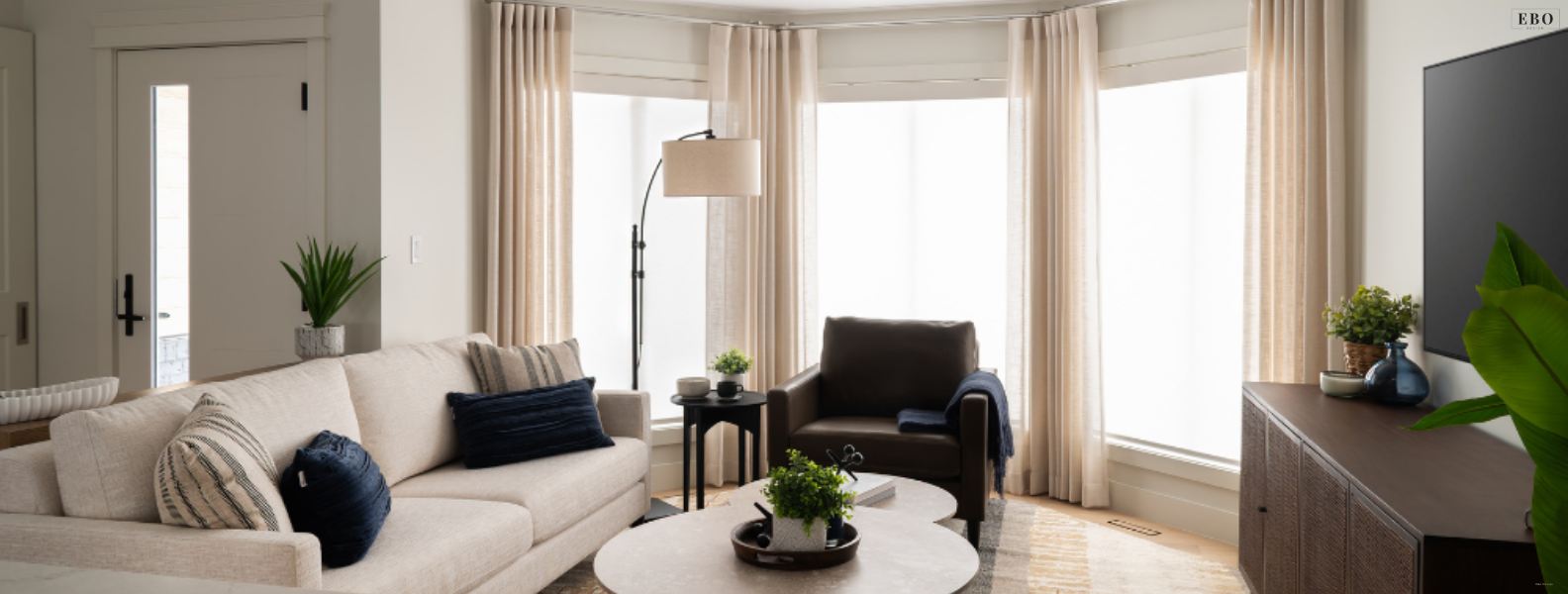 Bright, modern living room interior designed by EBO Design featuring a neutral sofa, navy accent pillows, custom drapery, and natural light.
