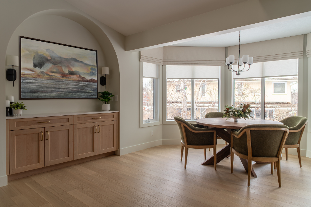 Modern dining room with a clear view through a bay window, round table, and green chairs.