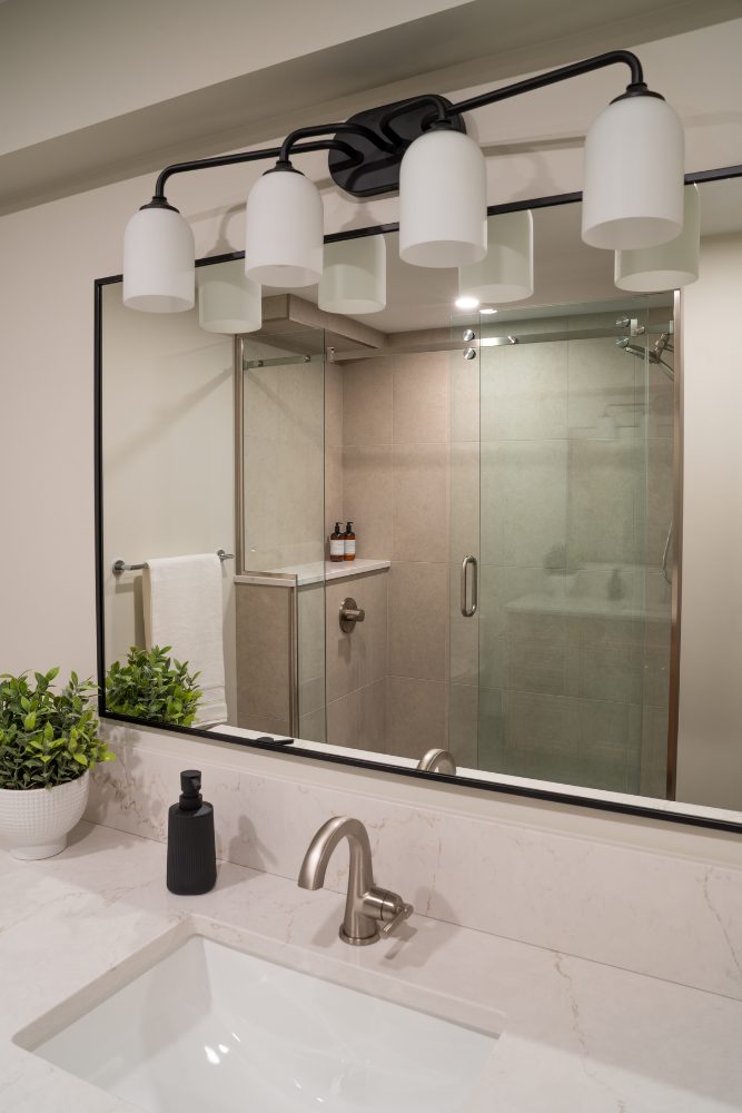 A modern bathroom vanity with a marble countertop, black-framed mirror, and multi-bulb light fixture.
