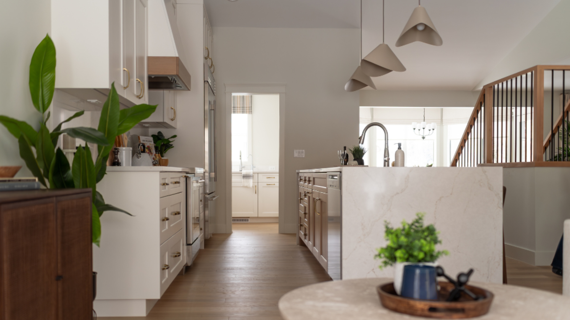 Open-plan home interior looking toward a modern kitchen with a waterfall quartz island, minimalist cone pendant lights, and house plants.