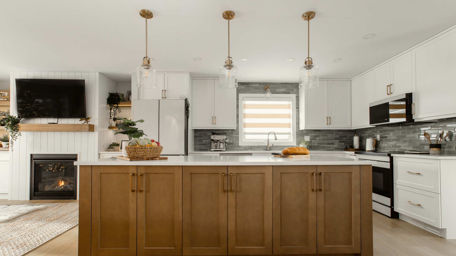 Modern kitchen featuring a warm wood island, glass pendant lighting, grey backsplash tile, and an open view to an adjacent living room fireplace.