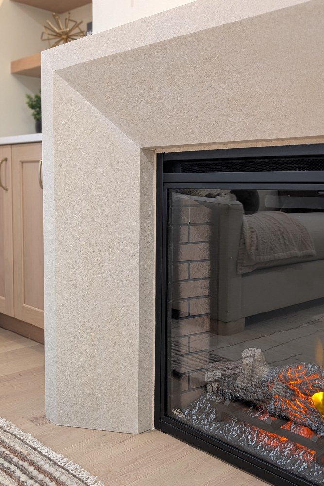 An angled close-up view of a modern electric fireplace with realistic glowing logs and a cast concrete mantelpiece.