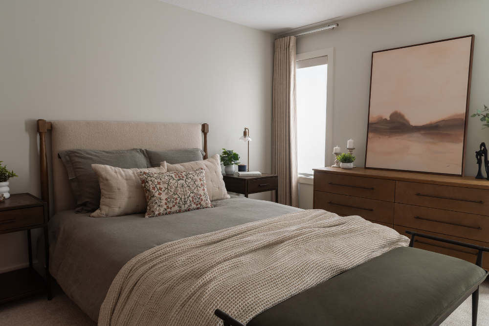 A peaceful modern bedroom with a beige upholstered headboard, green bedding, a decorative floral pillow, and dark wood nightstands.
