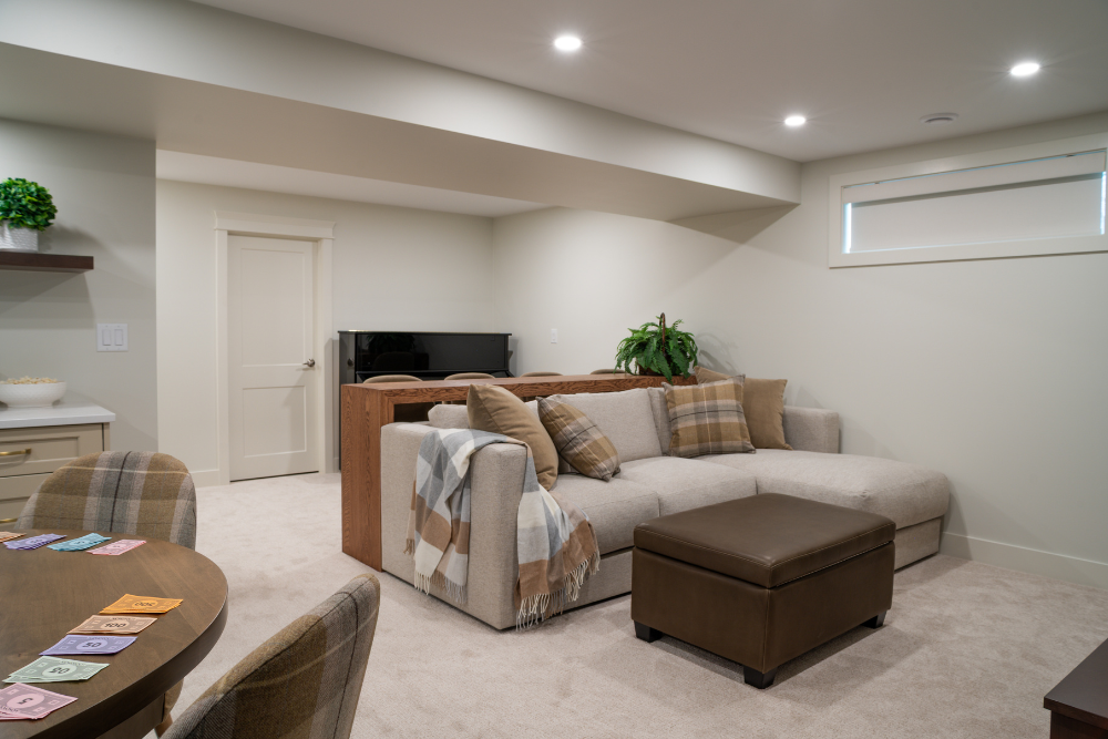 An expansive view of a basement recreation room with a gaming table, sectional sofa, and a kitchenette.