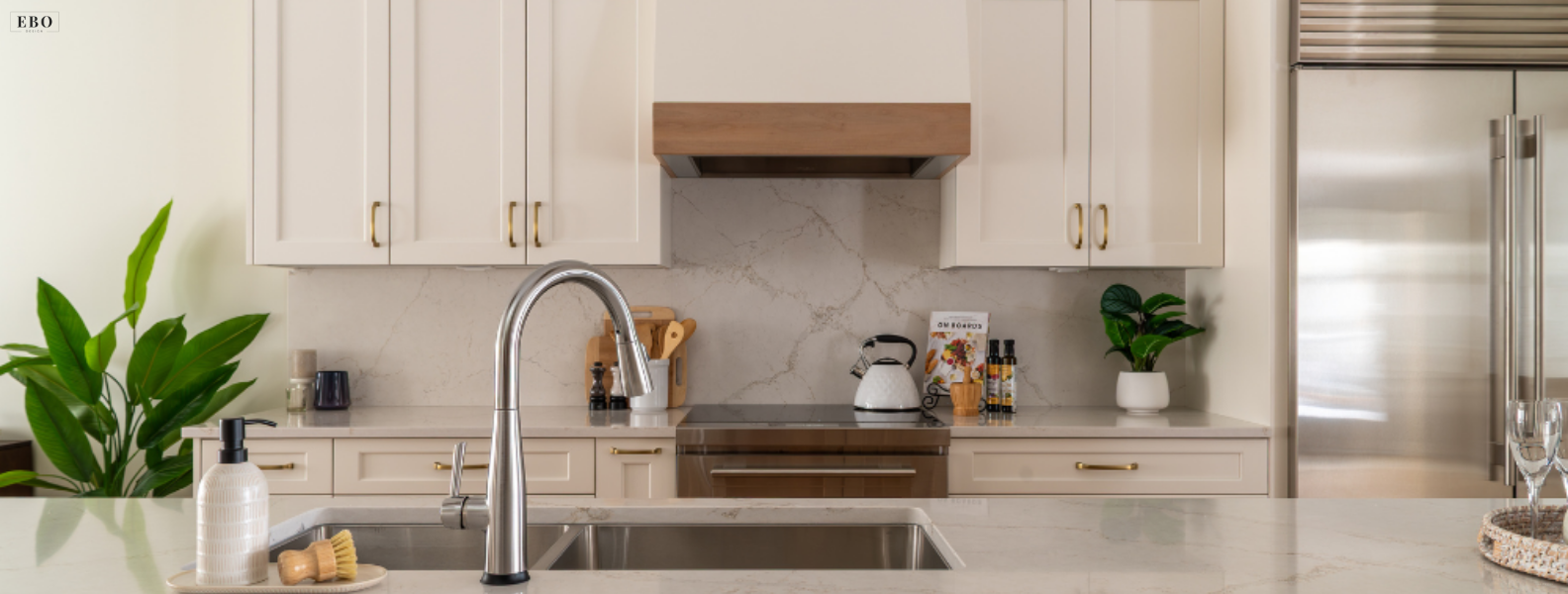 Modern white kitchen featuring brass hardware, custom wood range hood, stainless steel faucet, and marble-patterned quartz backsplash.