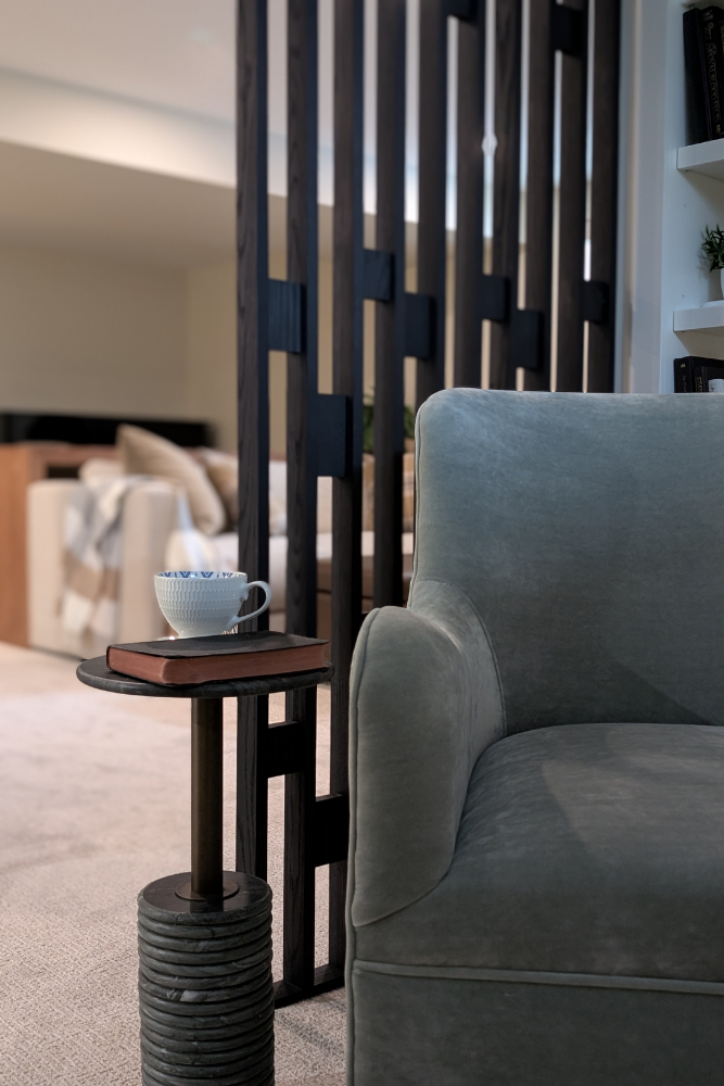 A cozy reading nook corner with a modern blue velvet armchair and a contemporary dark wood slat room divider, plus a side table with a cup.